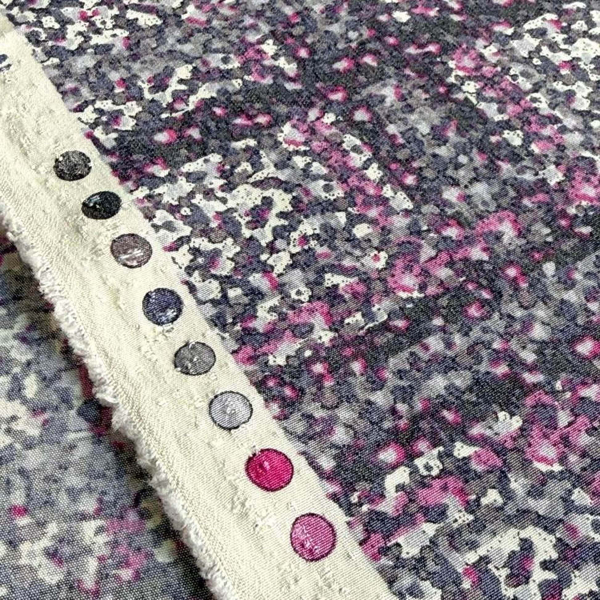 a close-up view of a fabric with a pattern of pink and purple dots, along with a white border.