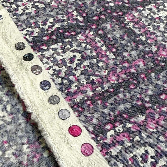 a close-up view of a fabric with a pattern of pink and purple dots, along with a white border.