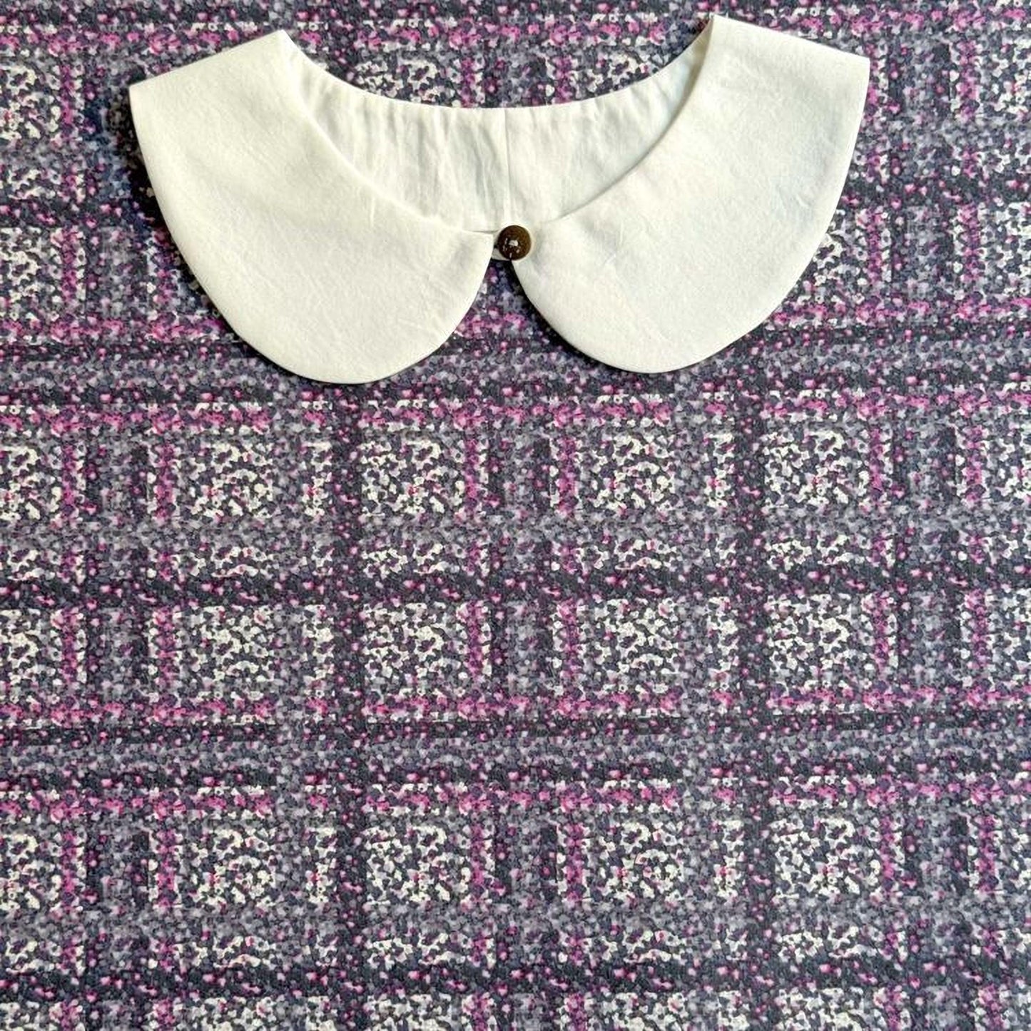 a white collar with a button, placed on a fabric with a floral pattern.
