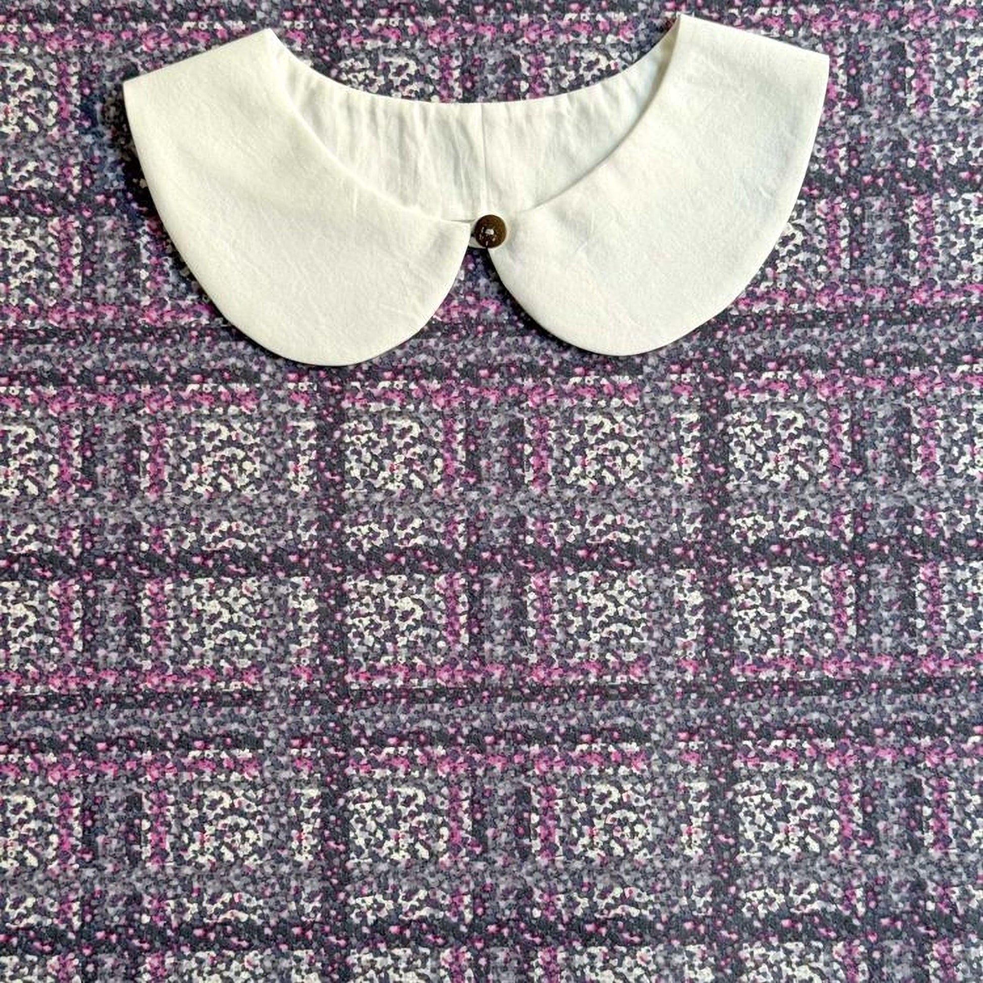 a white collar with a button, placed on a fabric with a floral pattern.