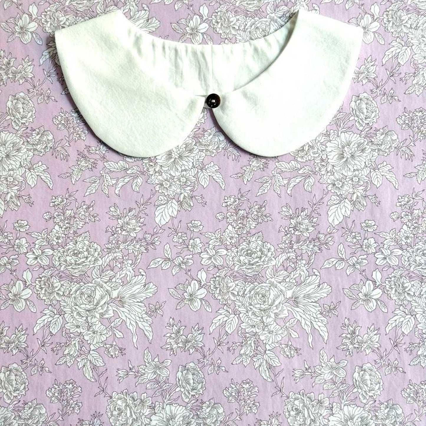 a white collar with a button, placed on a pink floral fabric background.