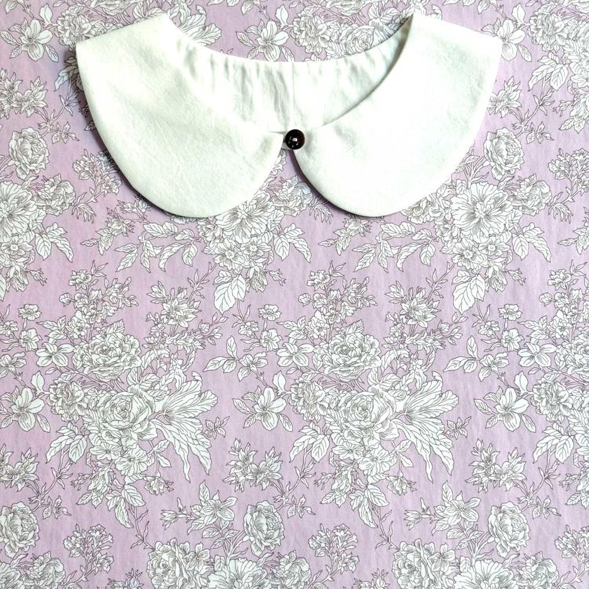 a white collar with a button, placed on a pink floral fabric background.