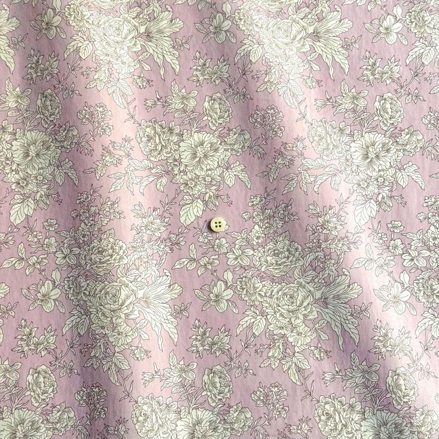 a close-up view of a fabric with a floral pattern in shades of pink and white. The fabric appears to be a piece of clothing, possibly a shirt or a dress, with a button visible in the center.