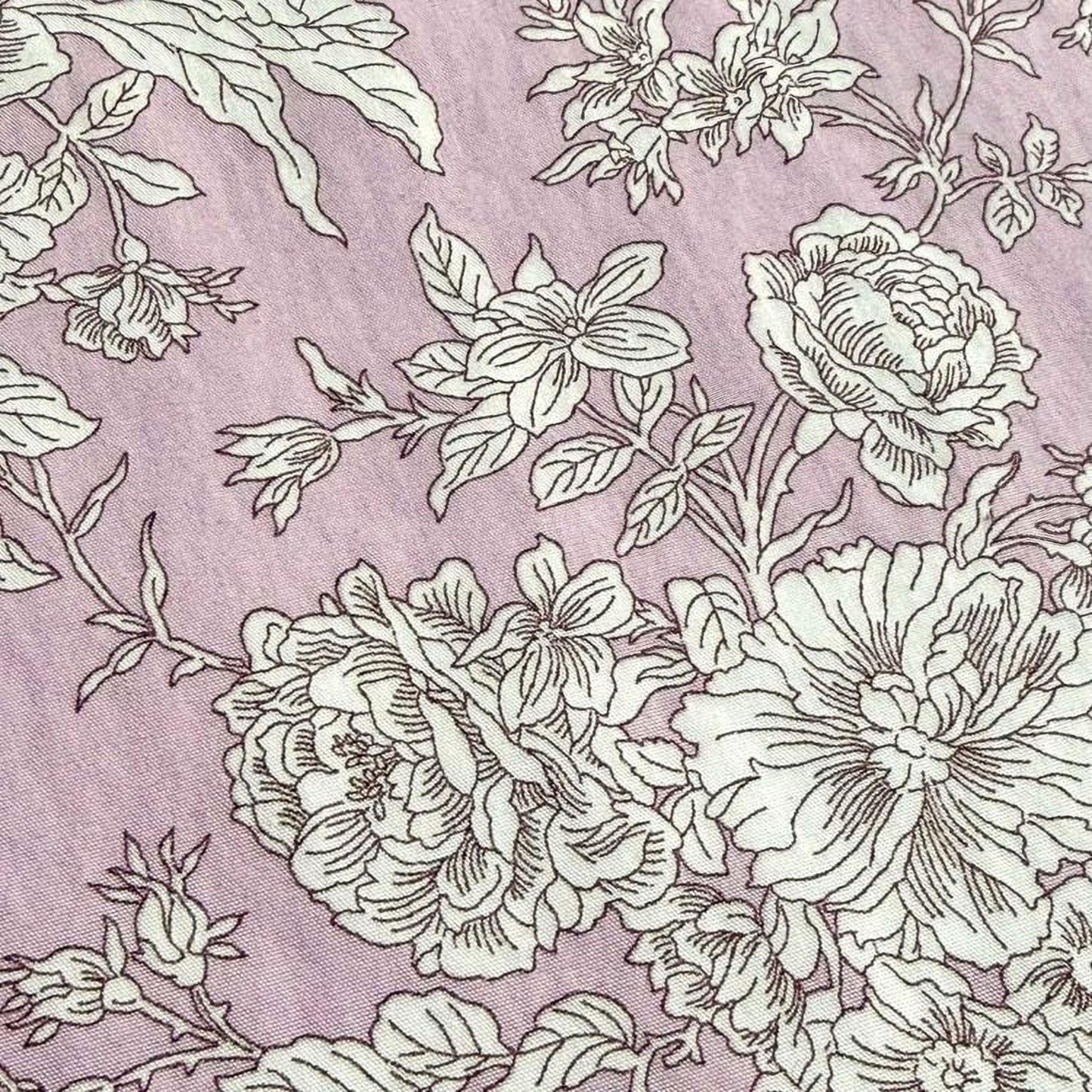 a close-up view of a fabric with a floral pattern in shades of pink and white. The pattern consists of various flowers and leaves, creating a visually appealing and intricate design.