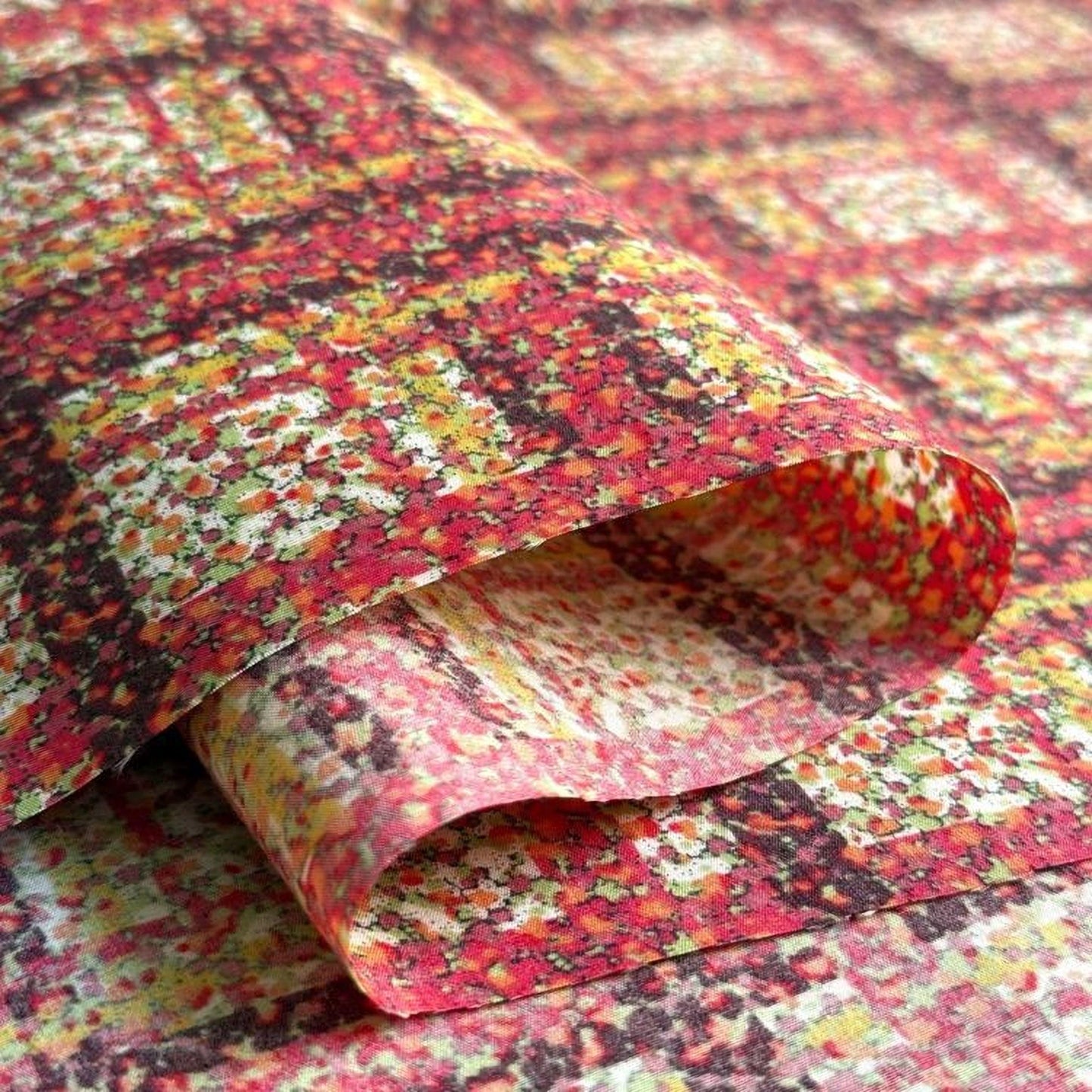 a close-up view of a colorful, abstract fabric with a pattern of red, yellow, and green colors. The fabric appears to be folded or rolled up, revealing its intricate design.