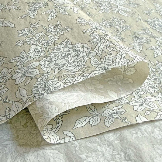 a close-up view of a fabric with a floral pattern, including white flowers and leaves. The fabric appears to be folded or rolled, revealing the intricate design underneath.
