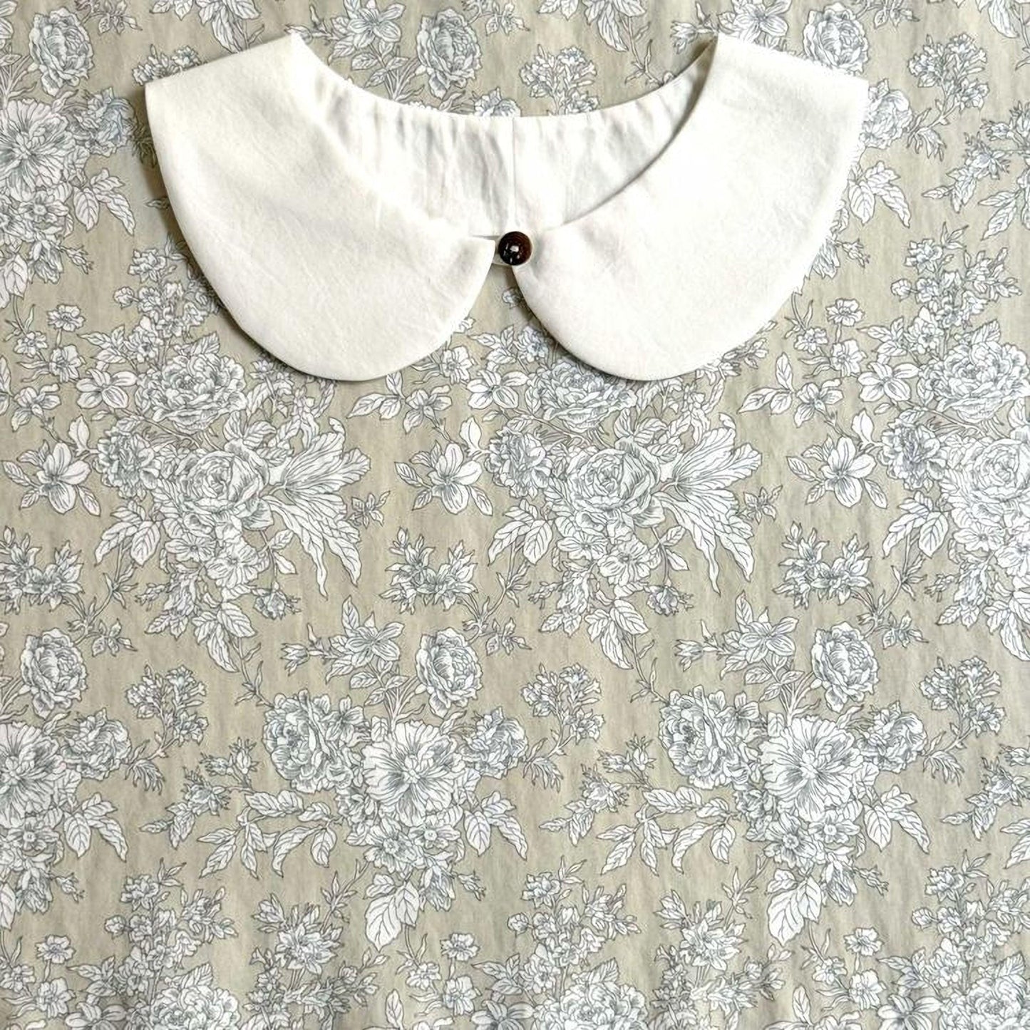a white collar with a button, set against a floral print background.