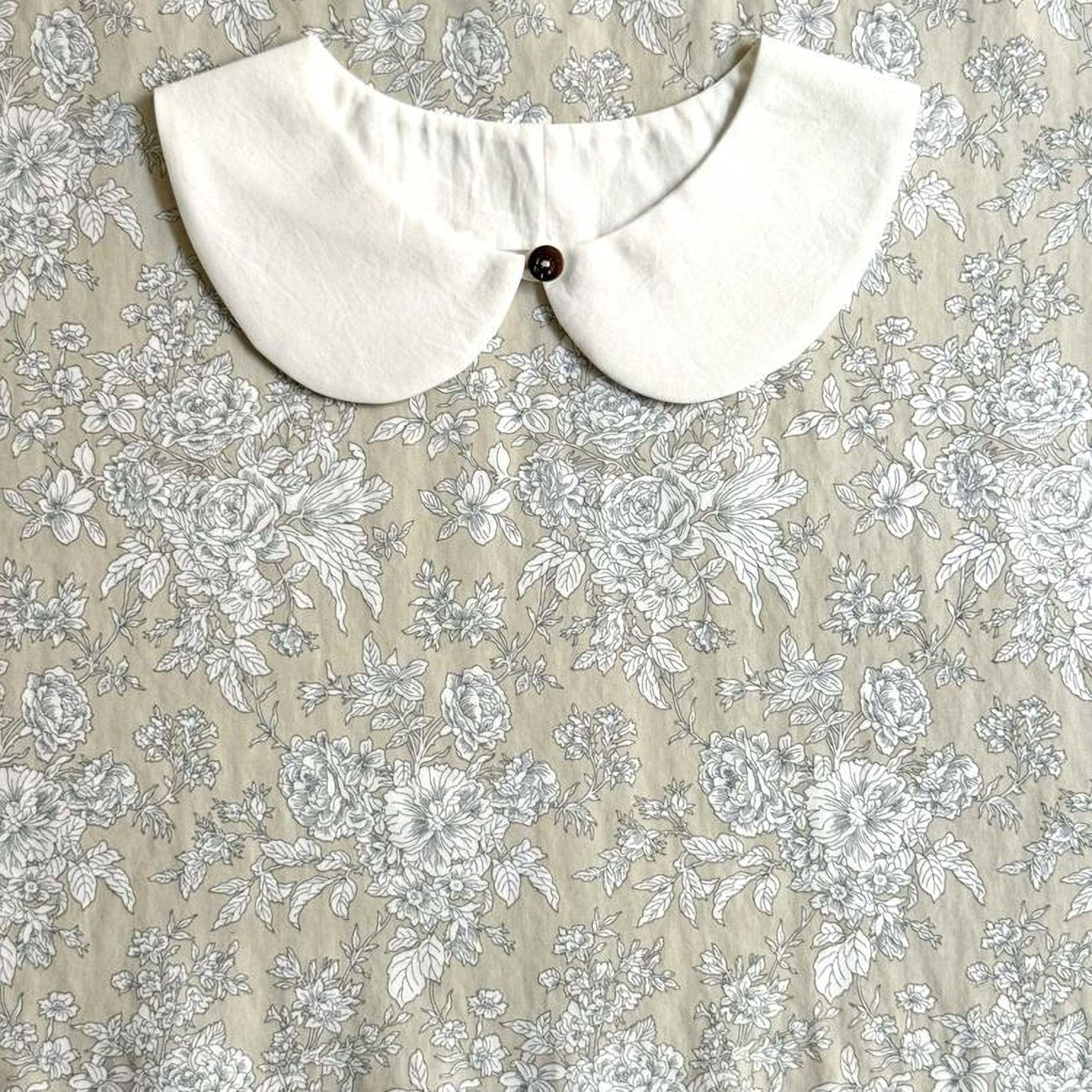 a white collar with a button, set against a floral print background.