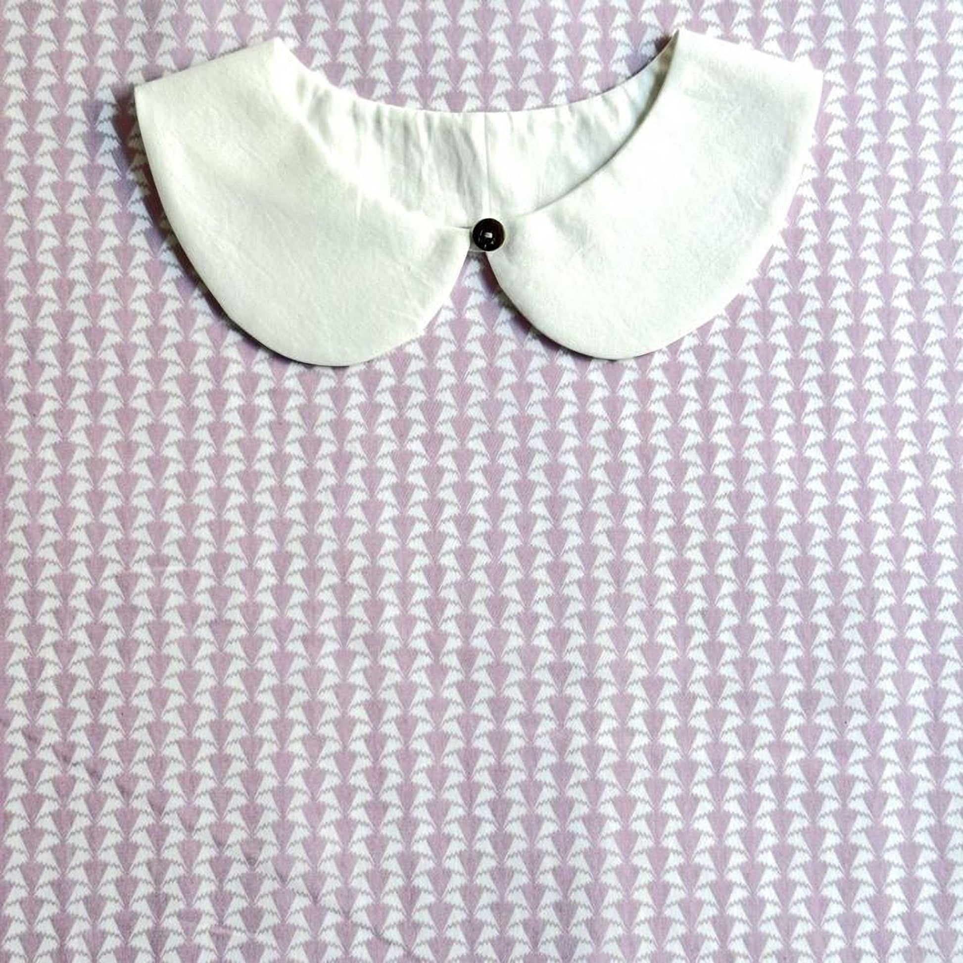 A white collar with a button is displayed against a purple and white patterned fabric background.