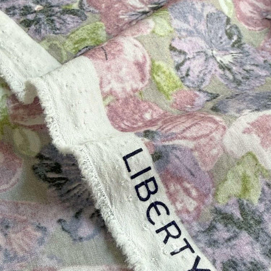 a close-up view of a fabric with a floral pattern, featuring a mix of pink, purple, and green colors. The fabric appears to be made of a soft, textured material, and there is a small, dark blue text visible on the fabric.