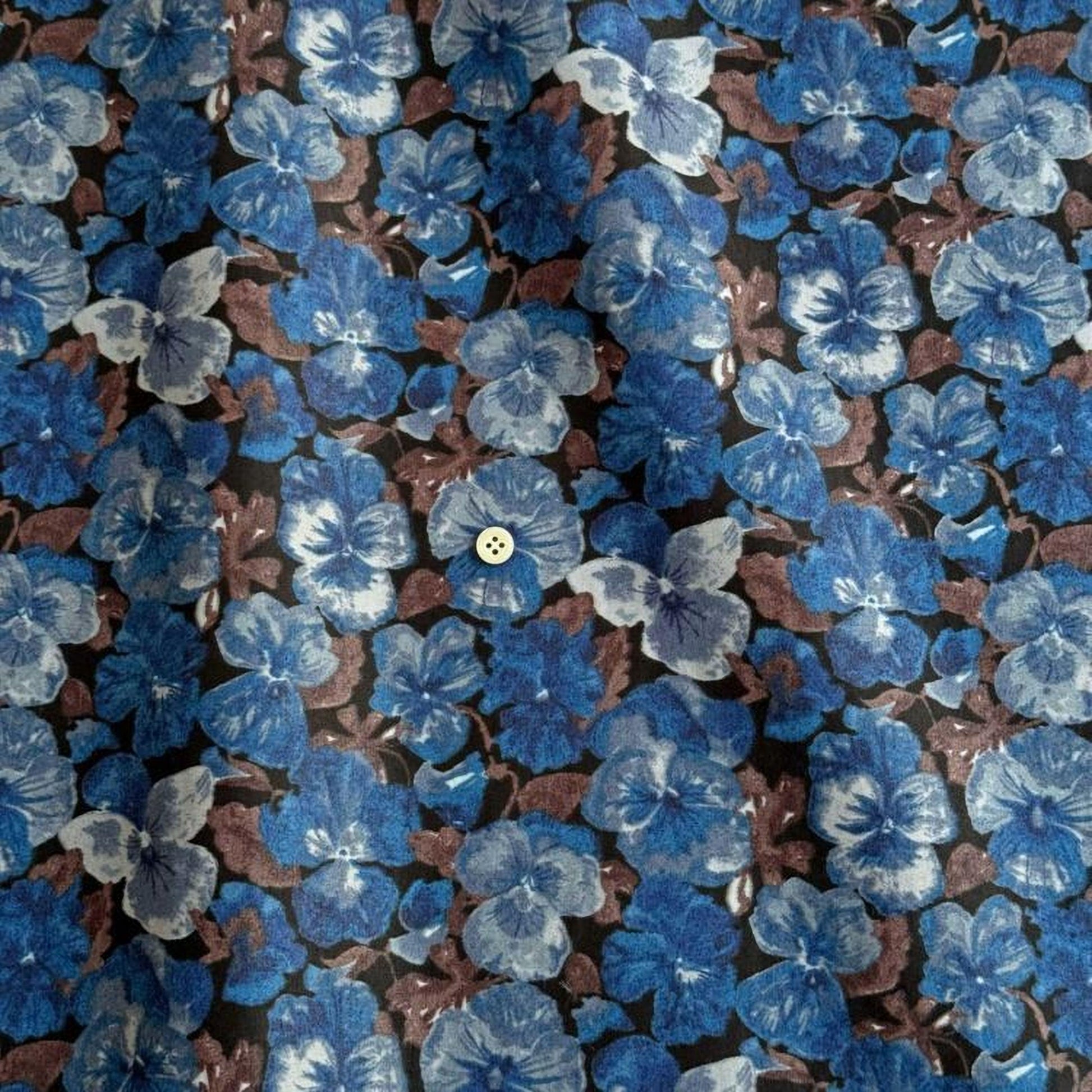 a close-up view of a fabric with a floral pattern in shades of blue and brown. The pattern consists of numerous small blue flowers interspersed with brown leaves, creating a visually striking and intricate design.