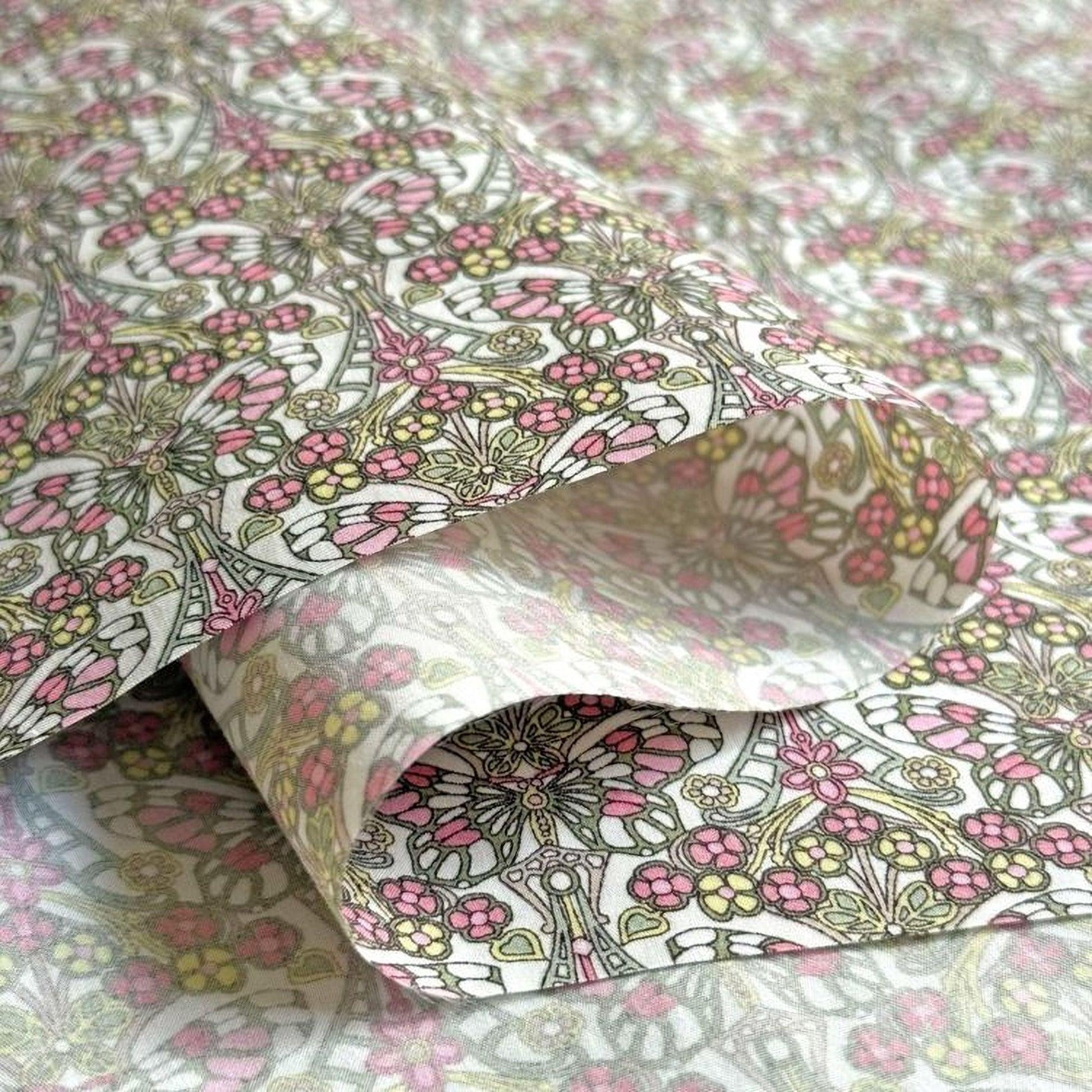 a close-up view of a fabric with a floral pattern in shades of pink, green, and yellow. The fabric appears to be folded or rolled, revealing the intricate design and texture of the pattern.