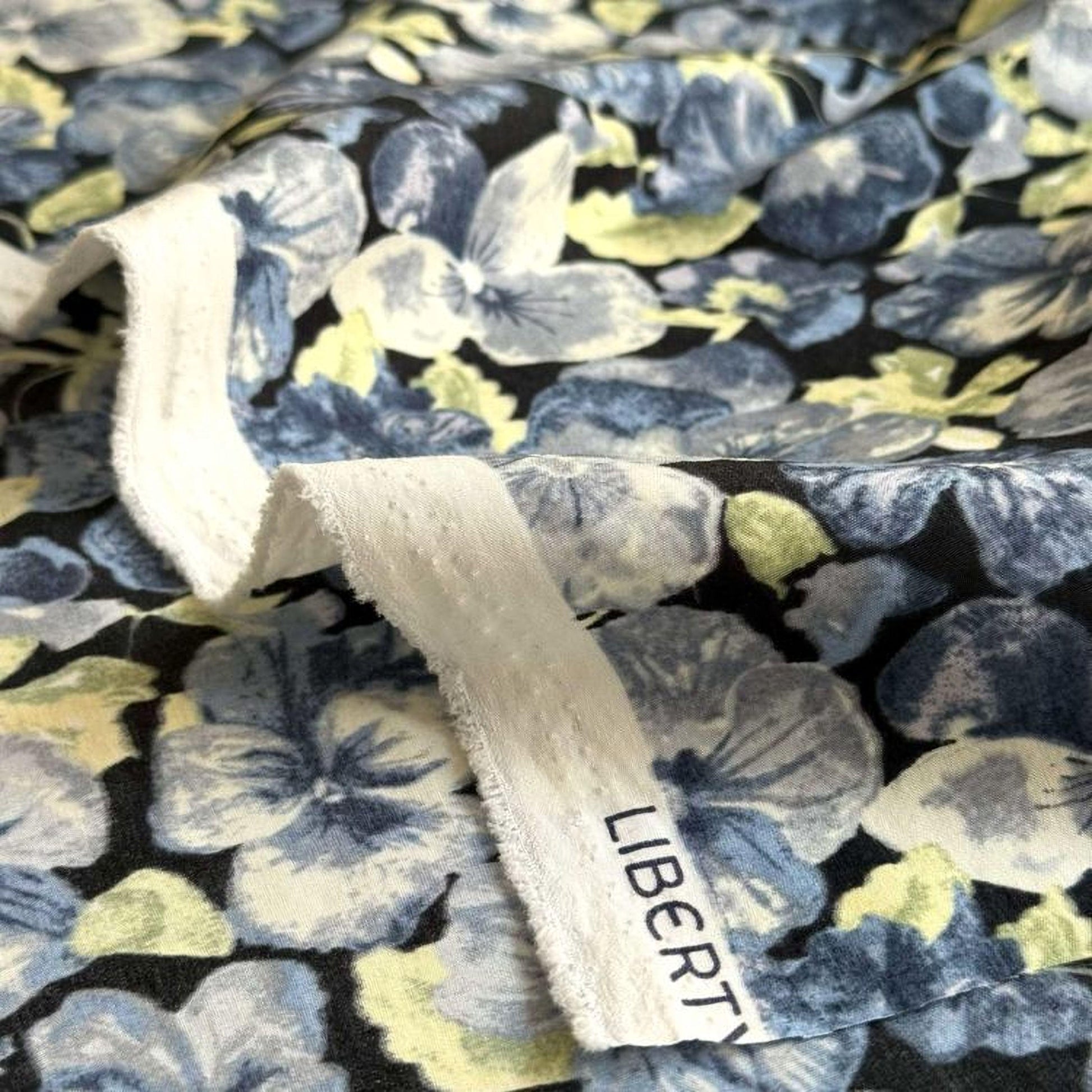 a close-up view of a fabric with a floral pattern in shades of blue and green. The fabric appears to be a dark-colored material with a white trim.