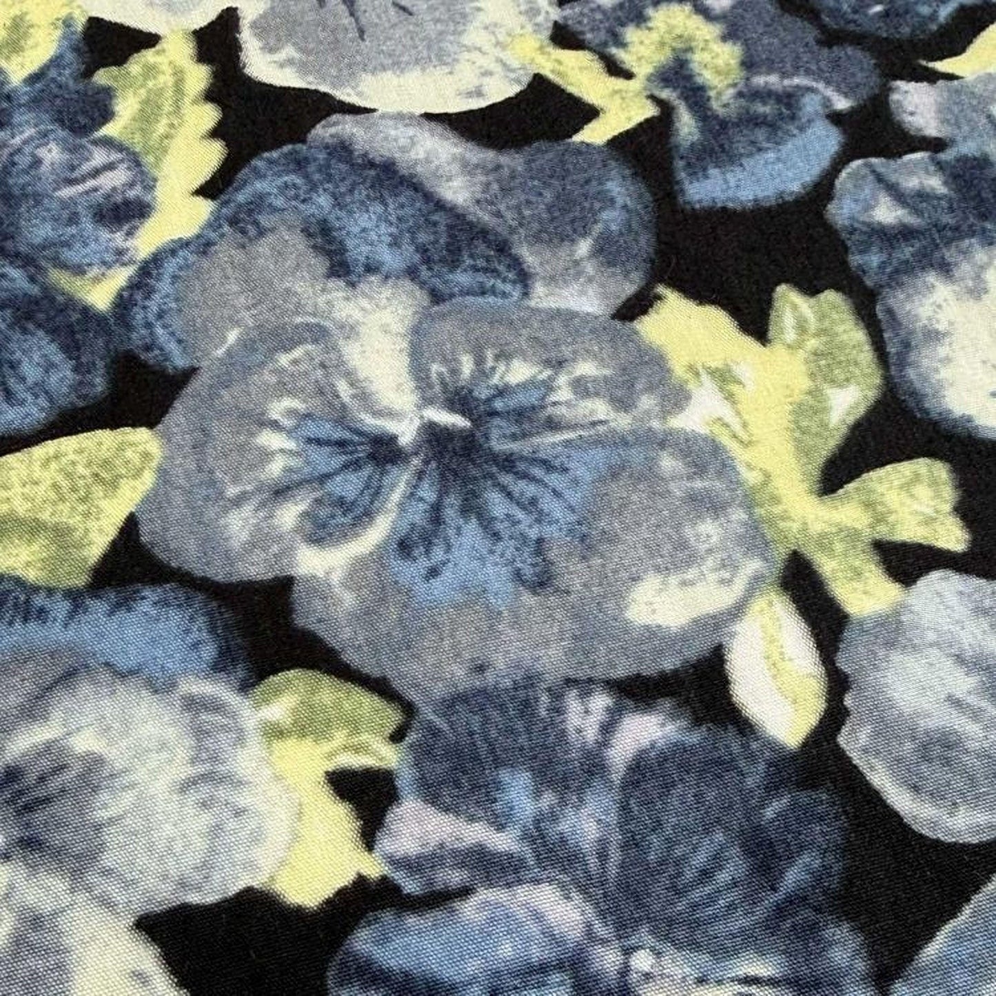 a close-up view of a fabric with a floral pattern in shades of blue and gray. The pattern consists of various flower-like shapes in different sizes and colors, creating a visually striking and intricate design.