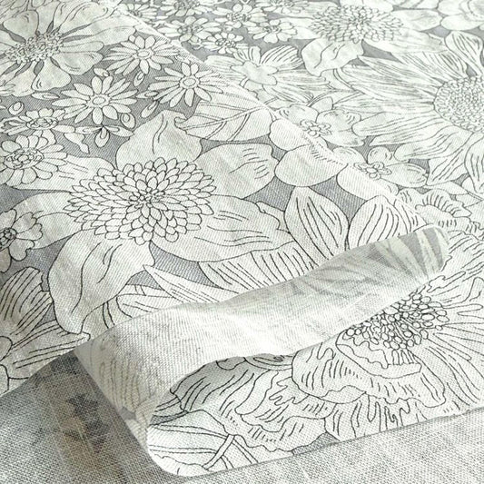 a close-up view of a fabric with a floral pattern, including various types of flowers and leaves. The fabric appears to be a piece of linens or a textile, with a gray and white color scheme.
