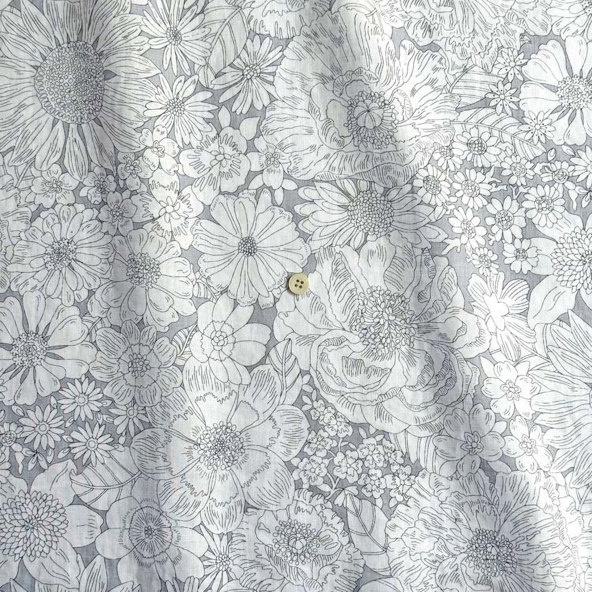 a close-up view of a fabric with a detailed floral pattern. The fabric appears to be a gray and white color scheme, with various types of flowers and leaves intricately designed and printed on it. There is a small button visible in the center of the fabric, adding a unique element to the overall design.
