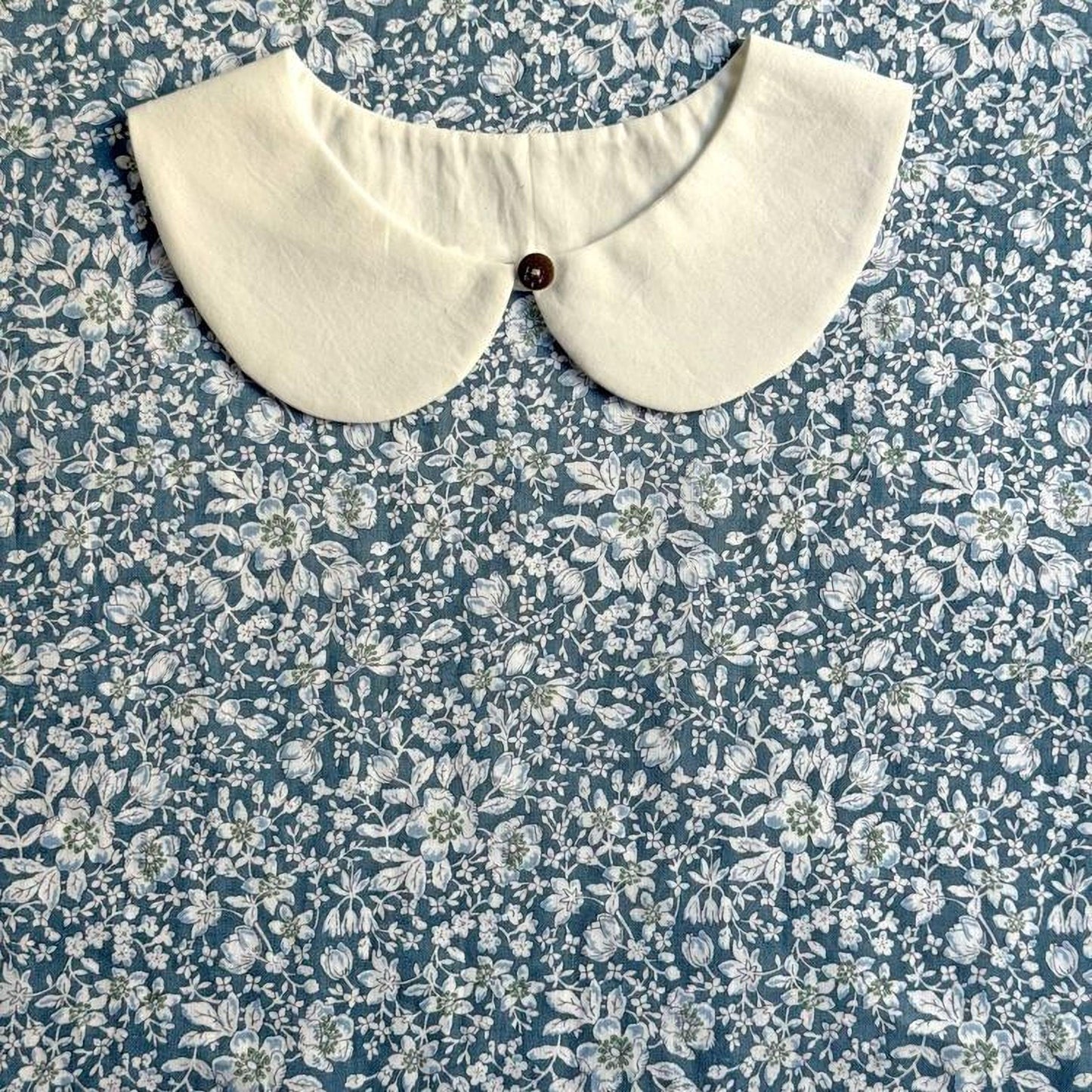 A white collar is displayed on a blue floral fabric background.