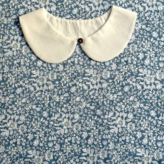 A white collar is displayed on a blue floral fabric background.