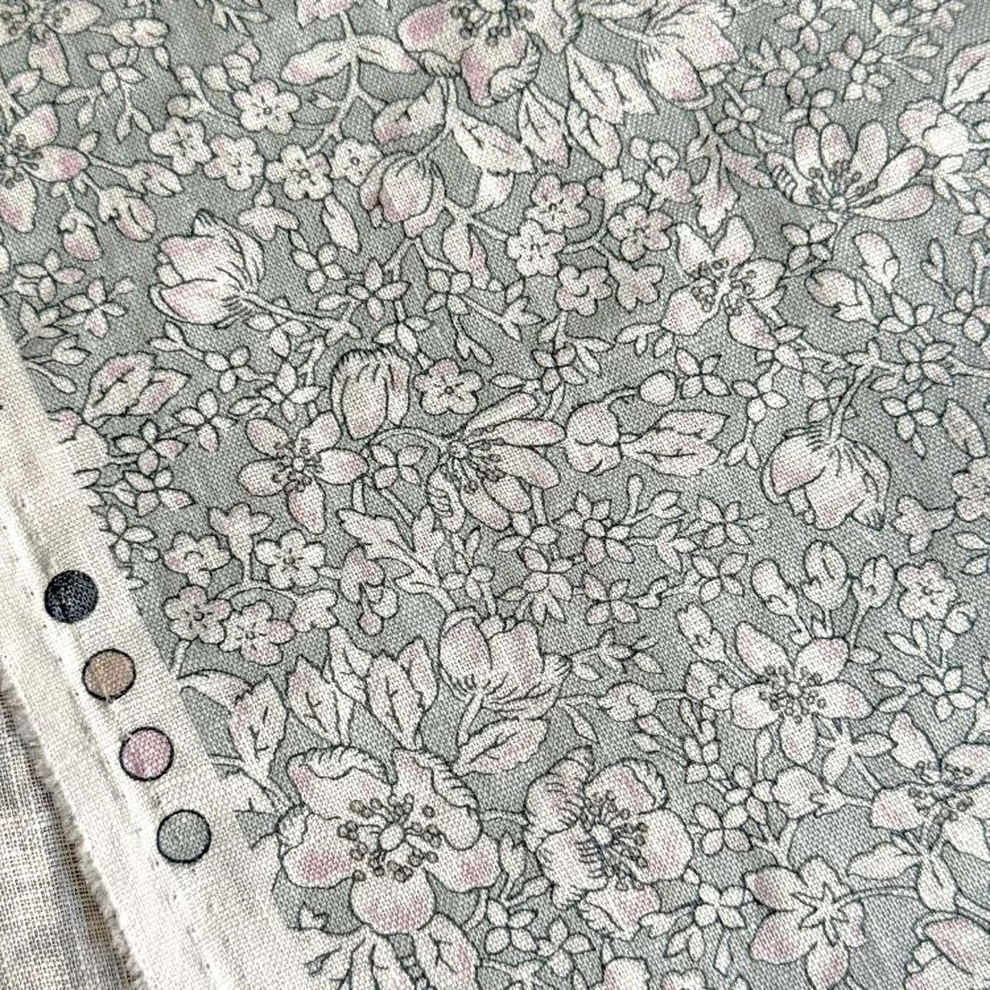 a close-up view of a fabric with a floral pattern, featuring various shades of gray and white flowers and leaves.