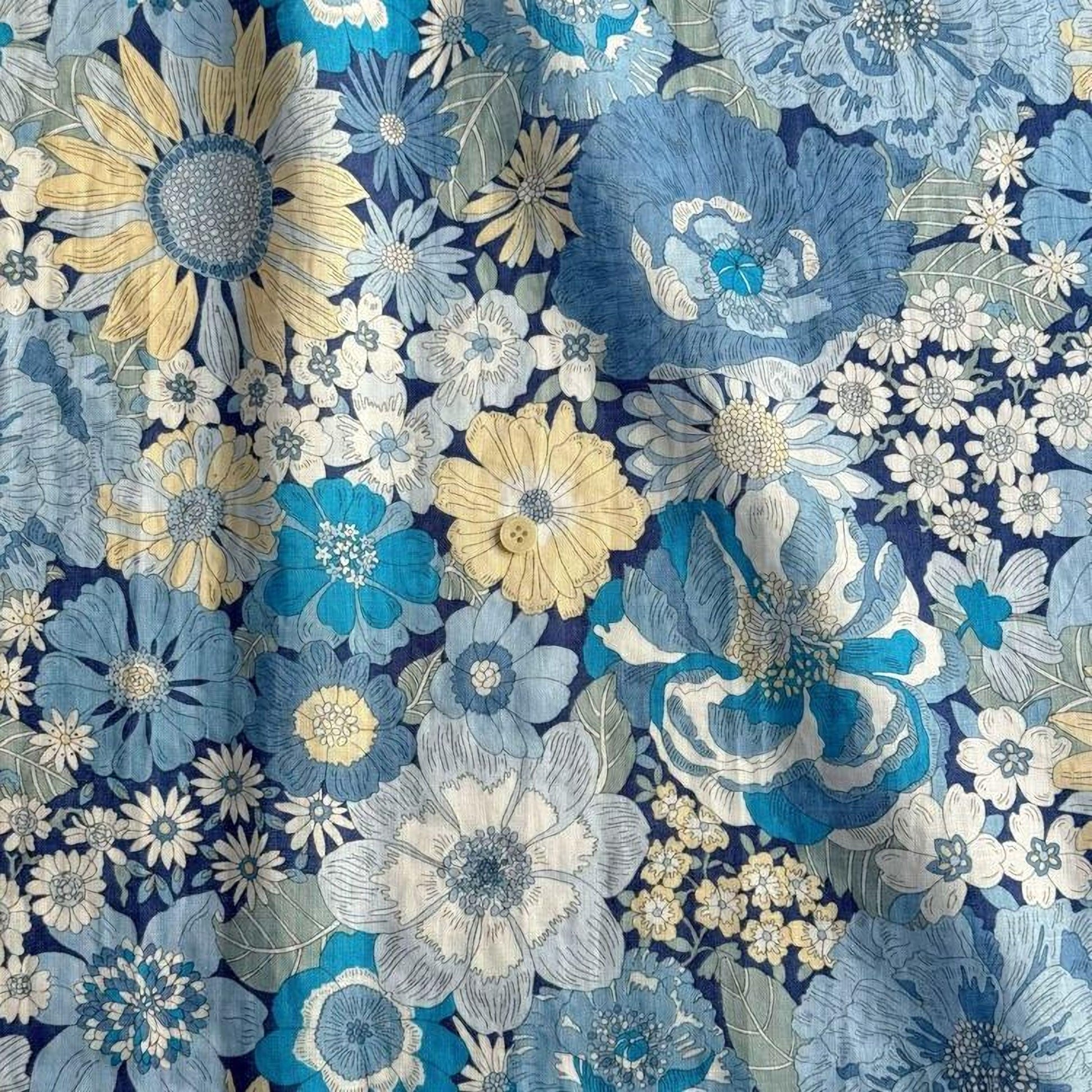 The image is a close-up of a fabric with a vibrant floral pattern in shades of blue, yellow, and white. The pattern features various types of flowers, including sunflowers, daisies, and other blooms, arranged in a visually appealing manner. The fabric appears to be a textile or material with a floral design, likely used for clothing or home decor.