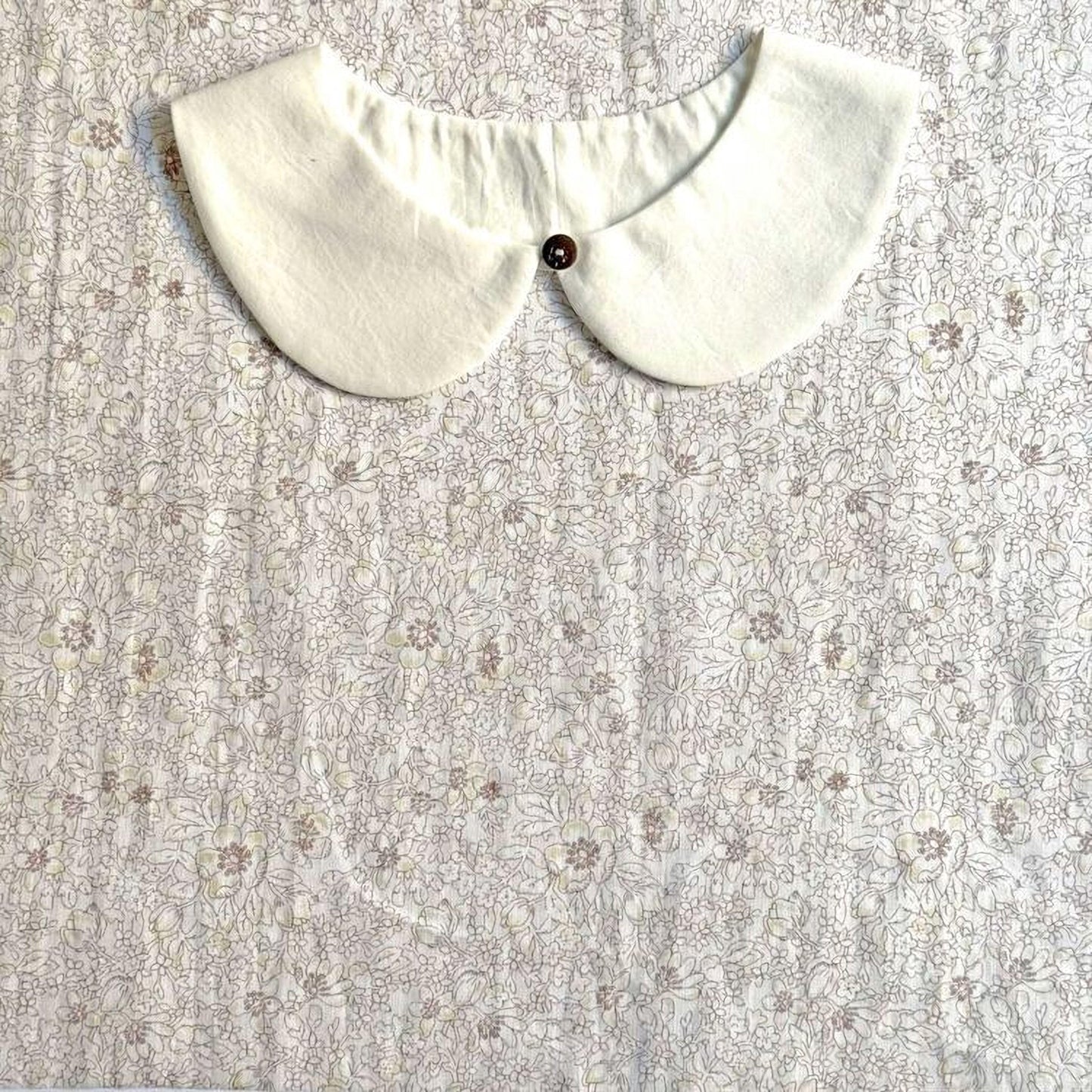 A white collar with a button is displayed on a fabric with a floral pattern.