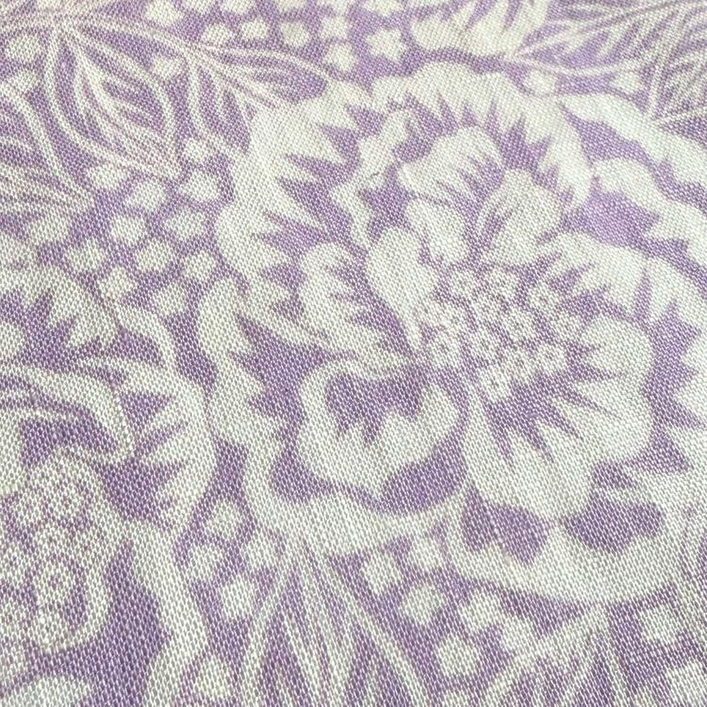 a close-up view of a fabric with a floral pattern in shades of purple and white. The pattern consists of various shapes and designs, including leaves, flowers, and other decorative elements, creating a visually appealing and intricate design.