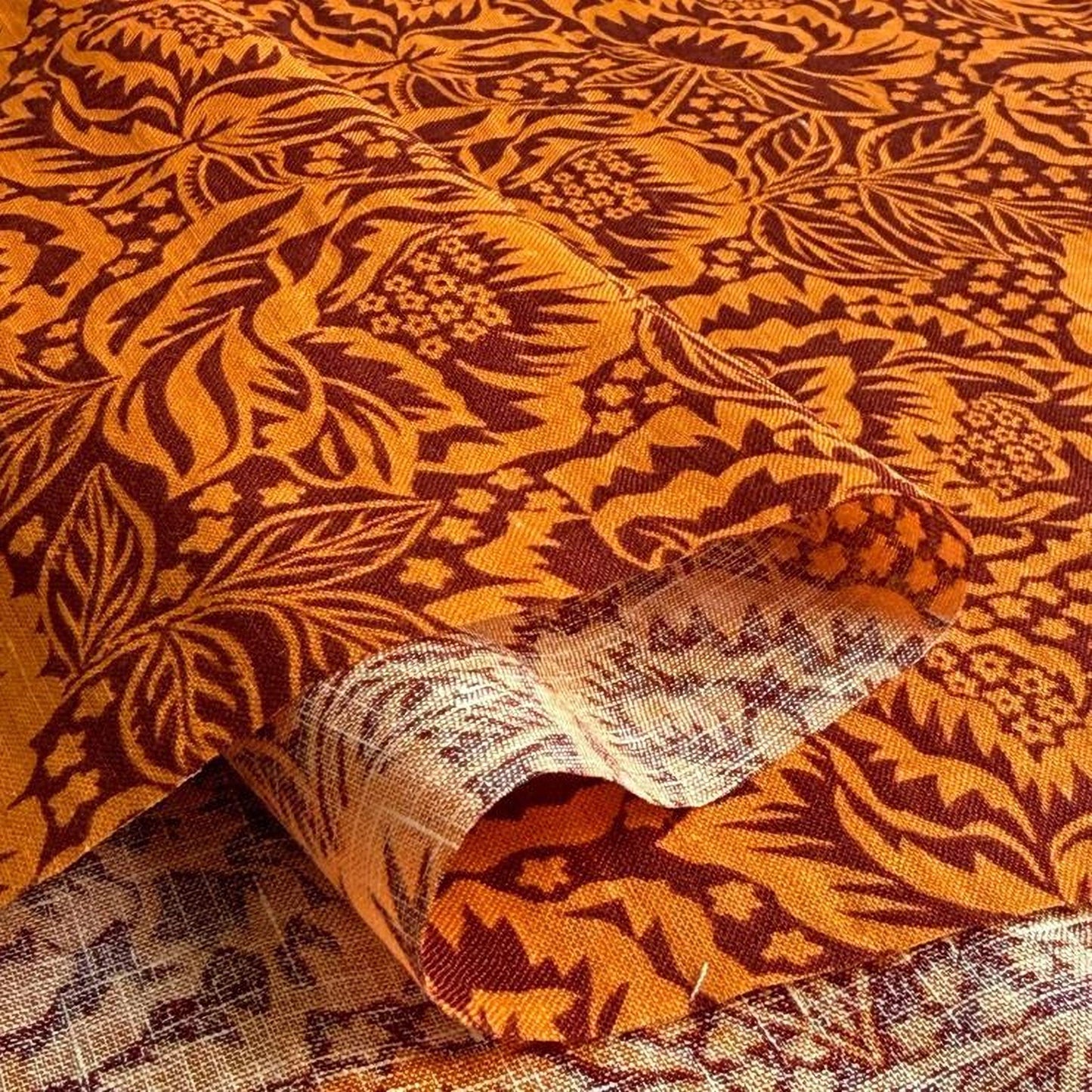 a close-up view of a fabric with a floral pattern in shades of orange and brown. The fabric appears to be folded or rolled, revealing its intricate design.