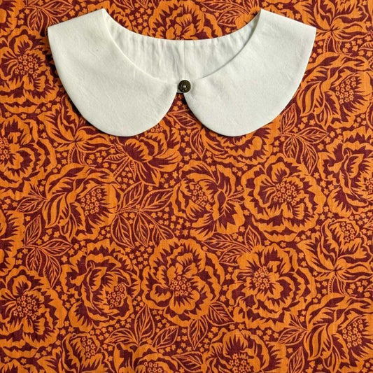 a white collar with a button, set against a background with a floral pattern in shades of orange and burgundy.