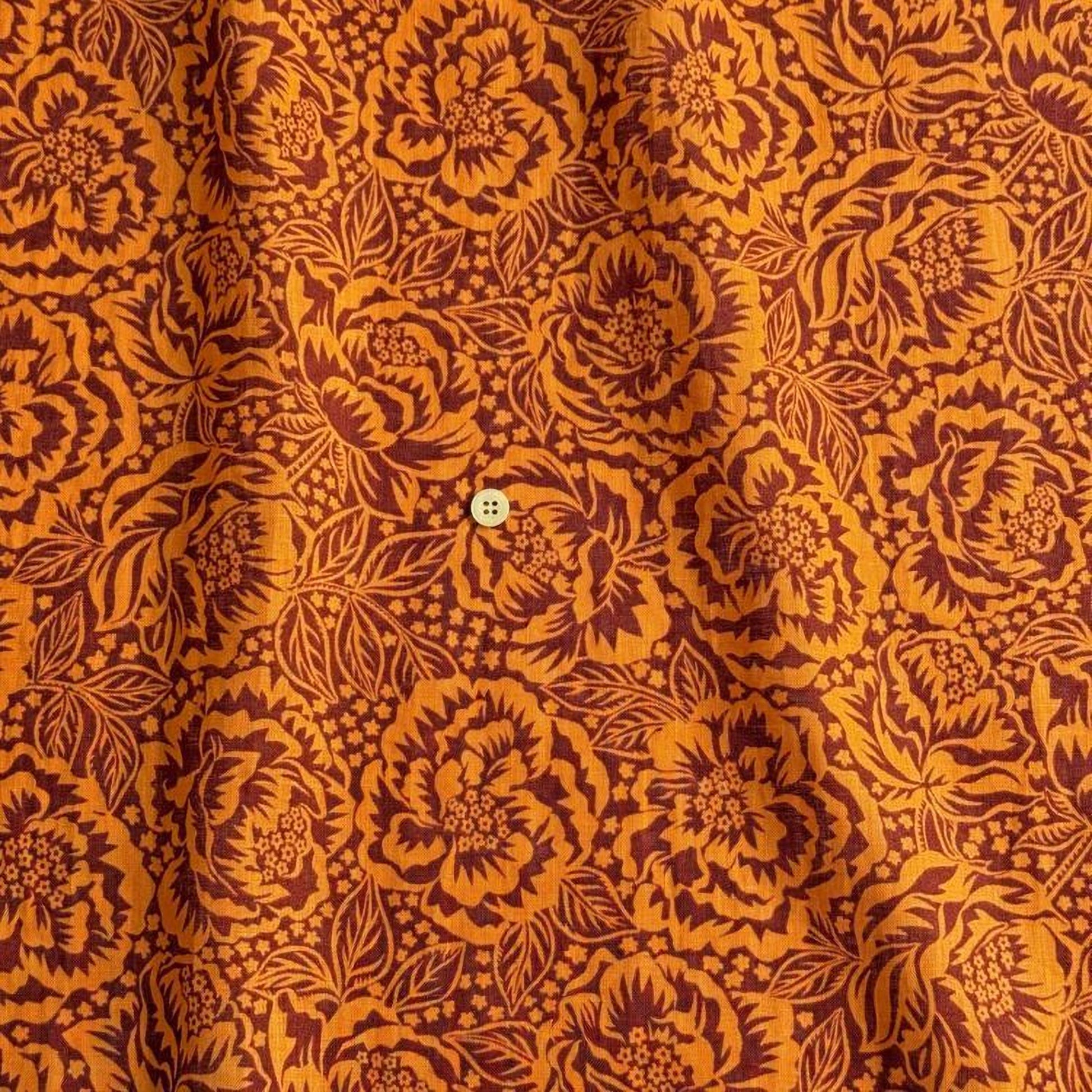 a close-up view of a fabric with a floral pattern in shades of orange and brown. The pattern is intricate and detailed, with numerous flowers and leaves covering the fabric. There is a small button visible in the center of the pattern.