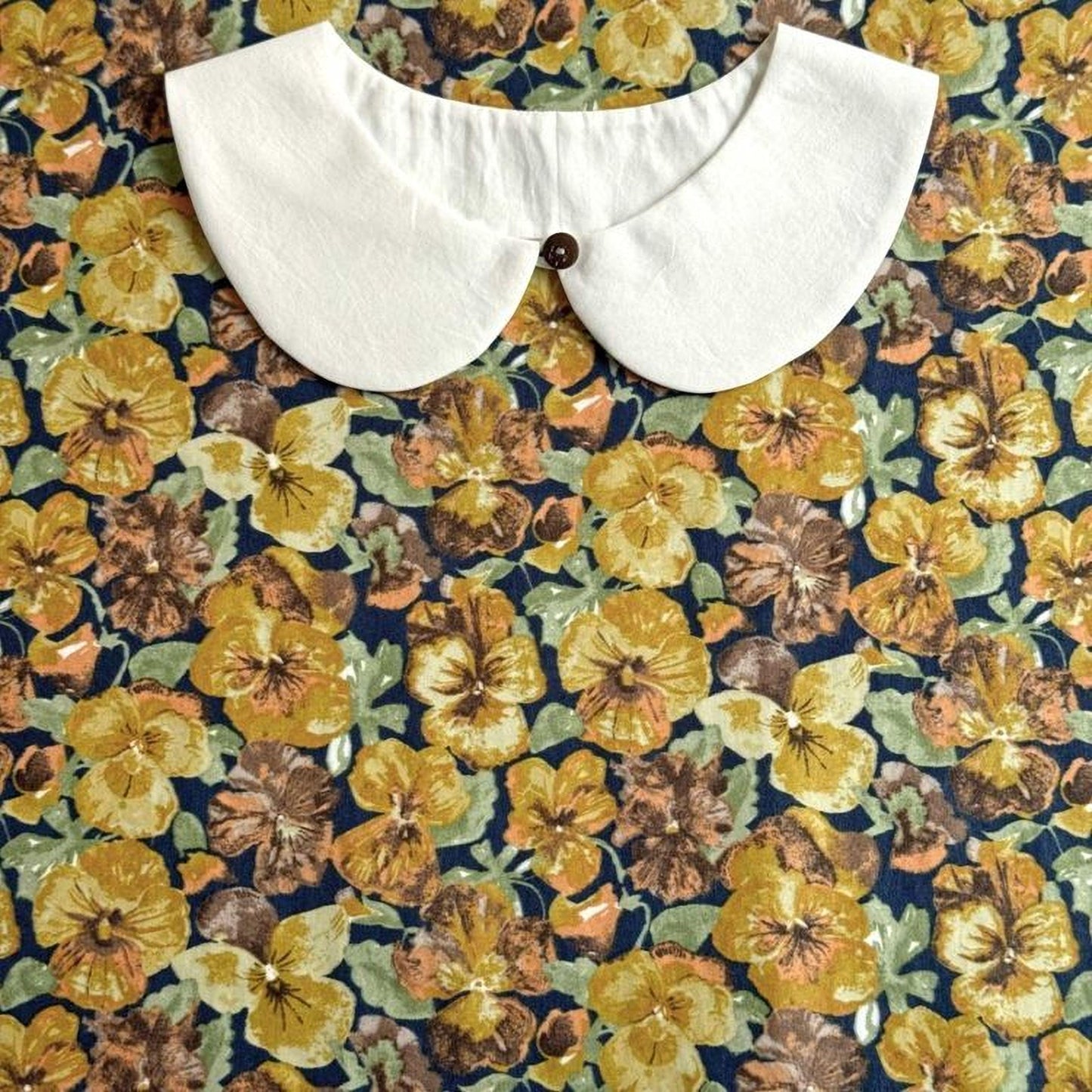 a white collar with a button, set against a background of a colorful floral print.