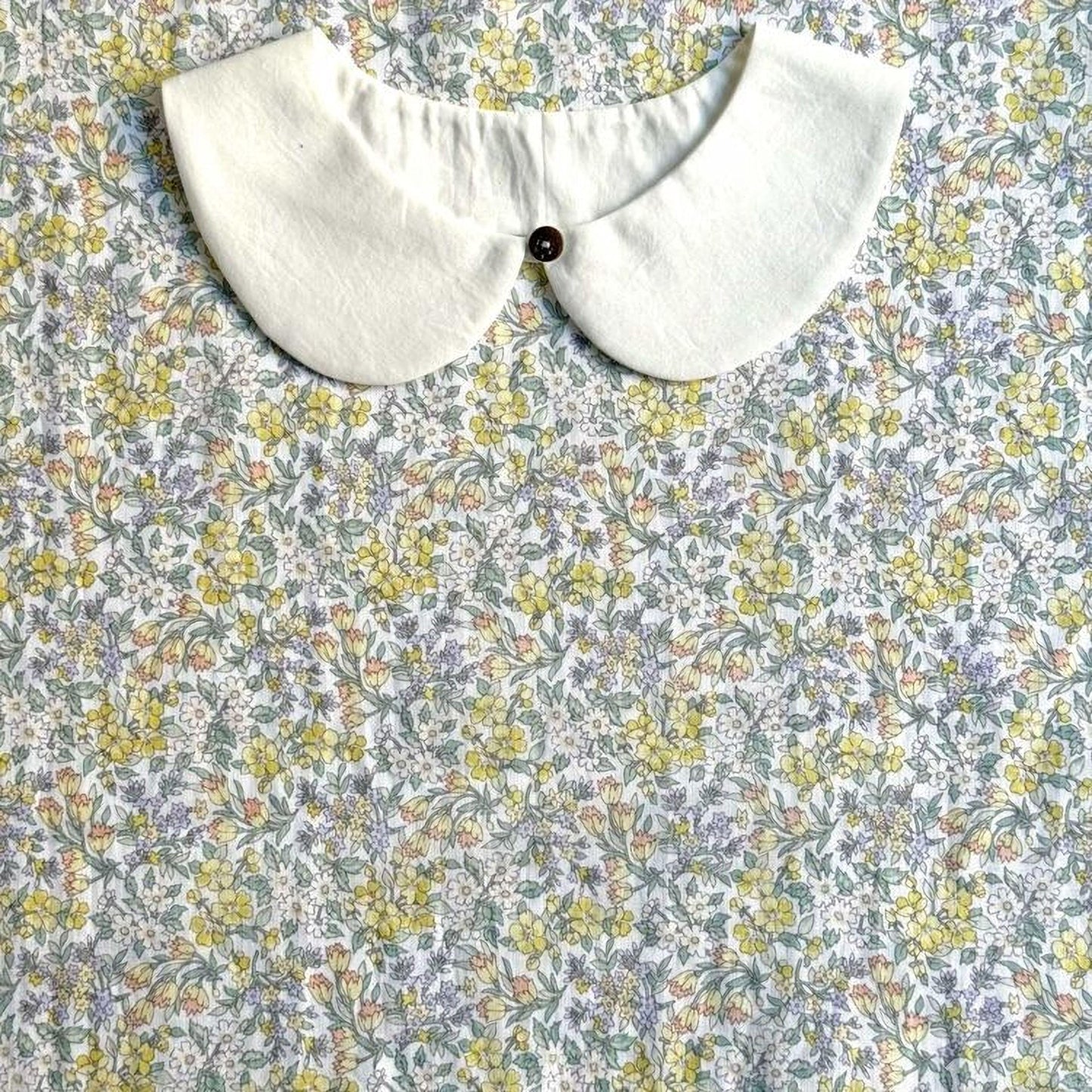 a white collar with a button, set against a background of a floral print fabric.