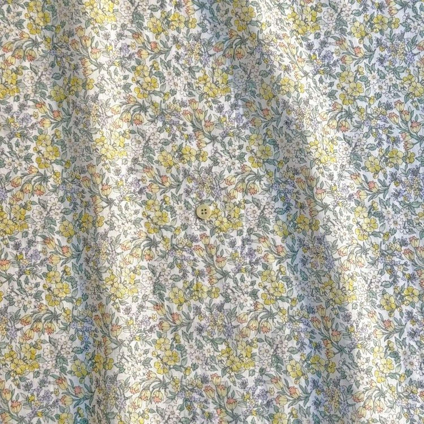 a close-up view of a fabric with a floral pattern, featuring yellow and green flowers. The fabric appears to be made of a soft, light-colored material, possibly cotton or linen. The pattern is intricate and detailed, with the flowers and leaves arranged in a repeating design across the fabric.