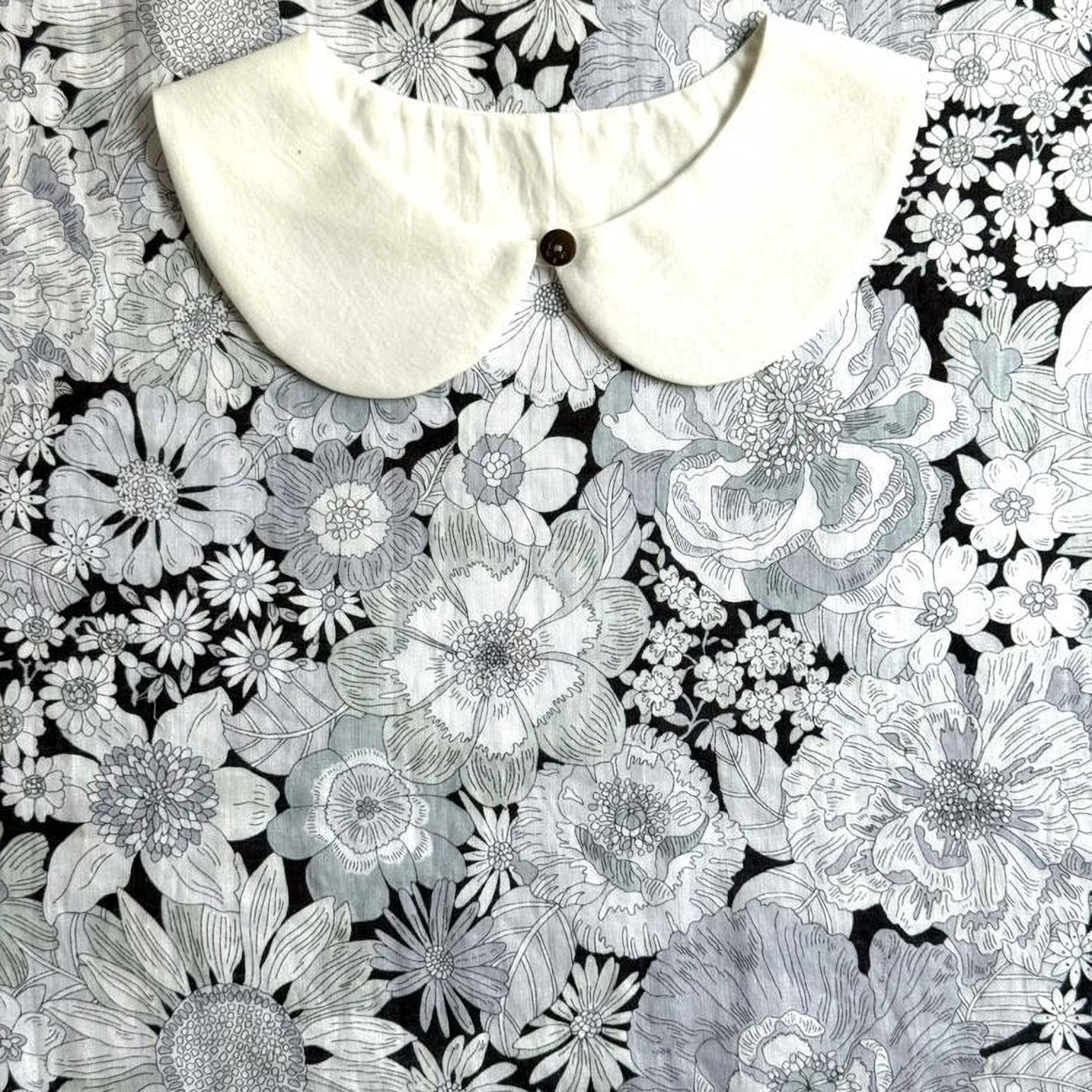 a white collar with a button, set against a background of a black and white floral pattern.