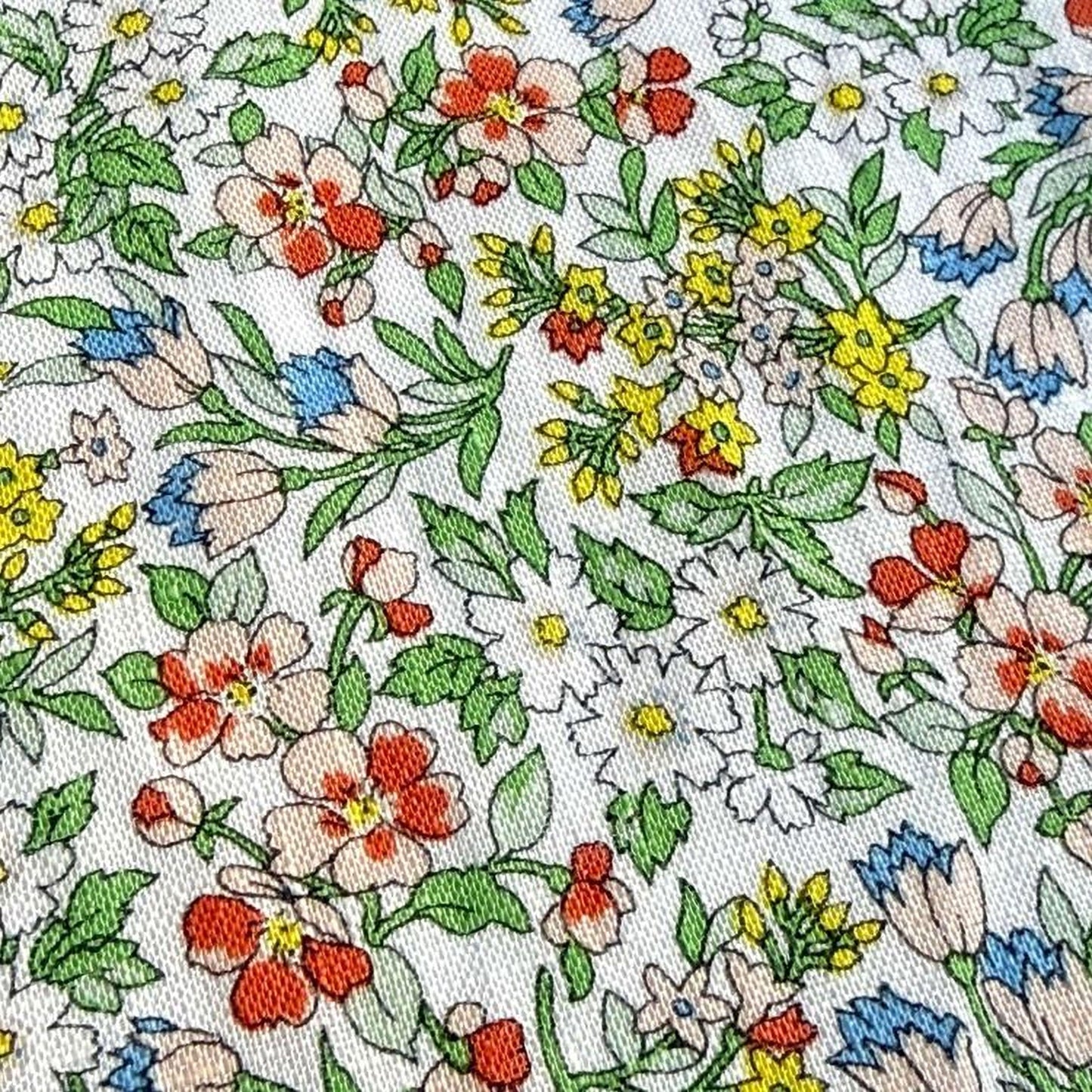 The image is a close-up of a fabric with a vibrant floral pattern. The pattern consists of various flowers and leaves in different colors, including red, yellow, white, and green. The flowers are arranged in a way that creates a visually appealing and intricate design.