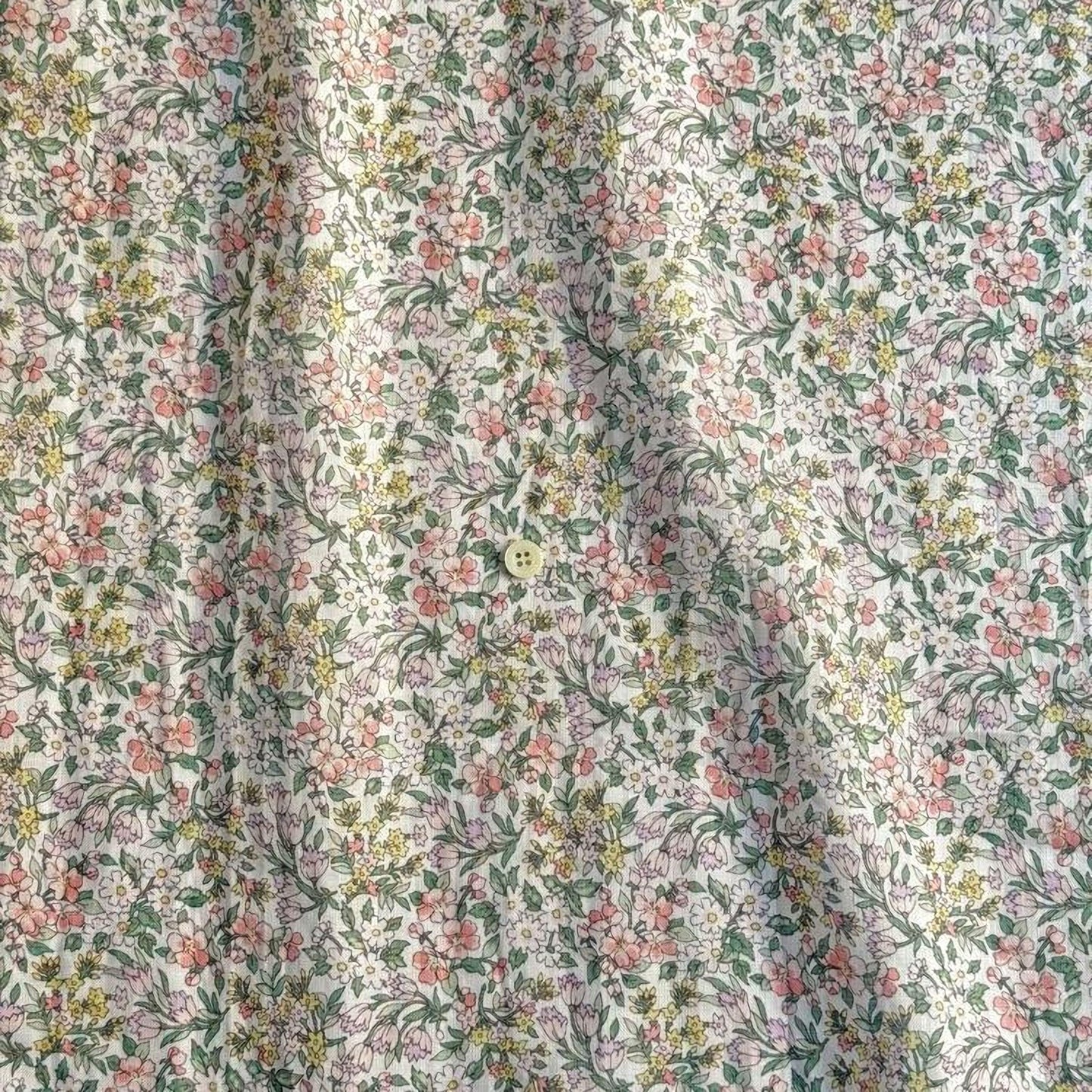 a close-up view of a fabric with a floral pattern, featuring a variety of colors including pink, green, yellow, and white. The fabric appears to be made of cotton and has a slightly wrinkled texture.