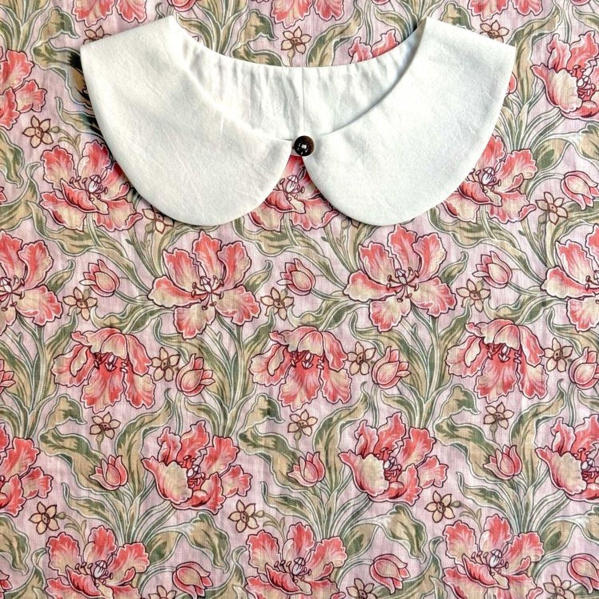 a white collar with a button, placed on a floral print fabric with pink and green flowers.