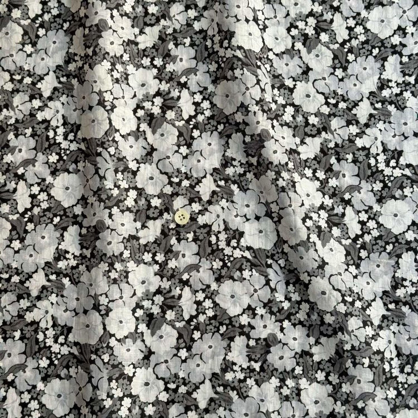 a close-up view of a fabric with a black and white floral pattern. The fabric appears to be made of a material with a floral design, and there is a small button visible in the center of the fabric.