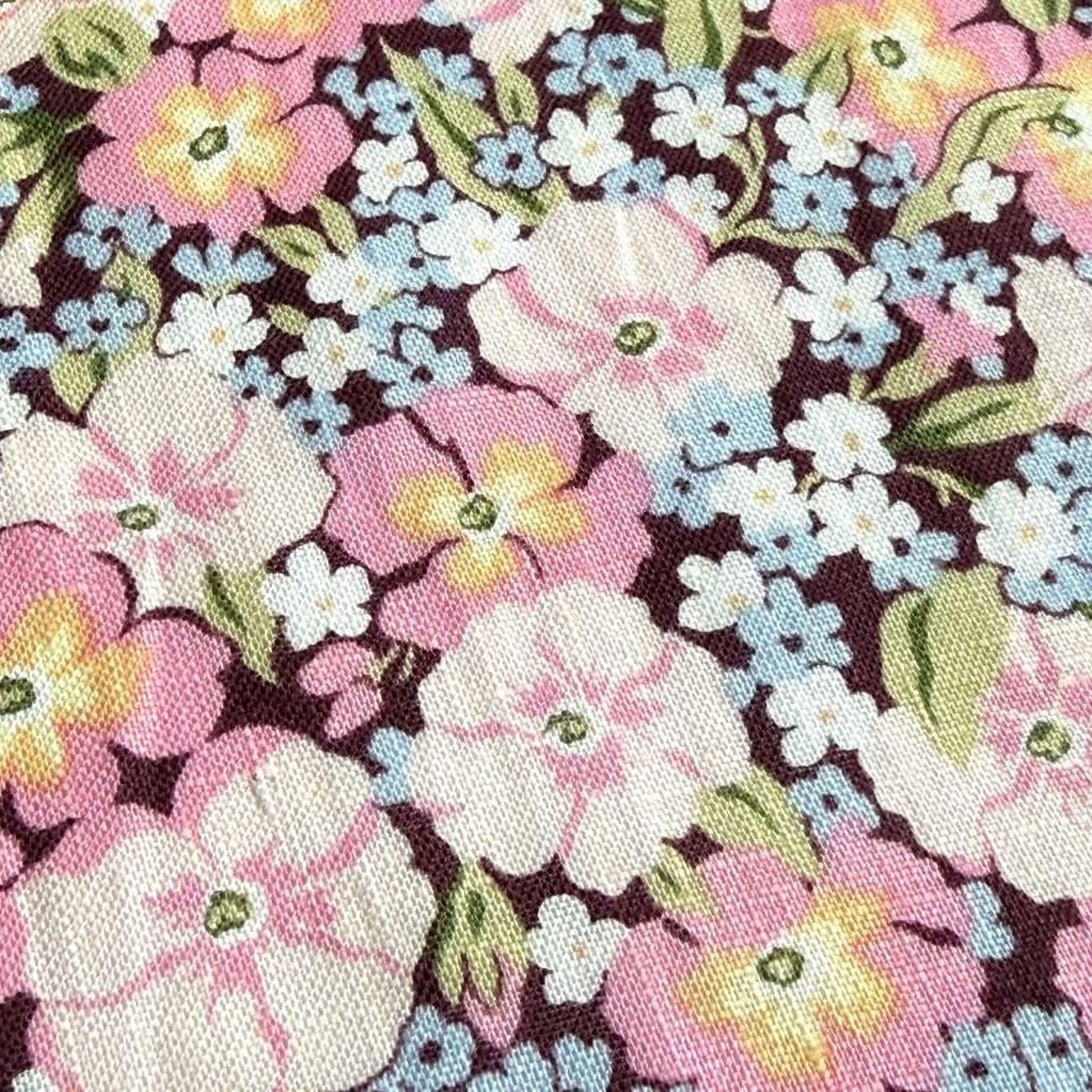 a close-up view of a fabric with a floral pattern. The fabric is adorned with a variety of colorful flowers, including pink, white, and blue flowers, as well as green leaves. The flowers are arranged in a visually appealing manner, creating a vibrant and lively design. The fabric appears to be made of a soft, textured material, which adds to its overall aesthetic appeal.