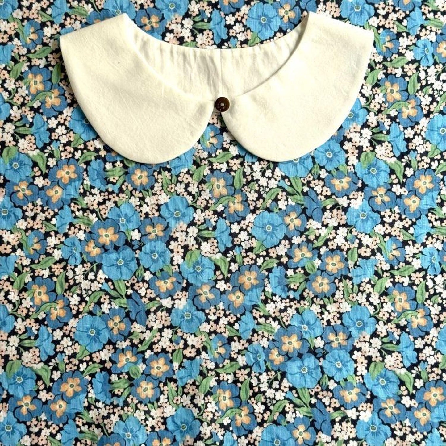a white collar with a button, set against a background of a floral print with blue, orange, and white flowers.