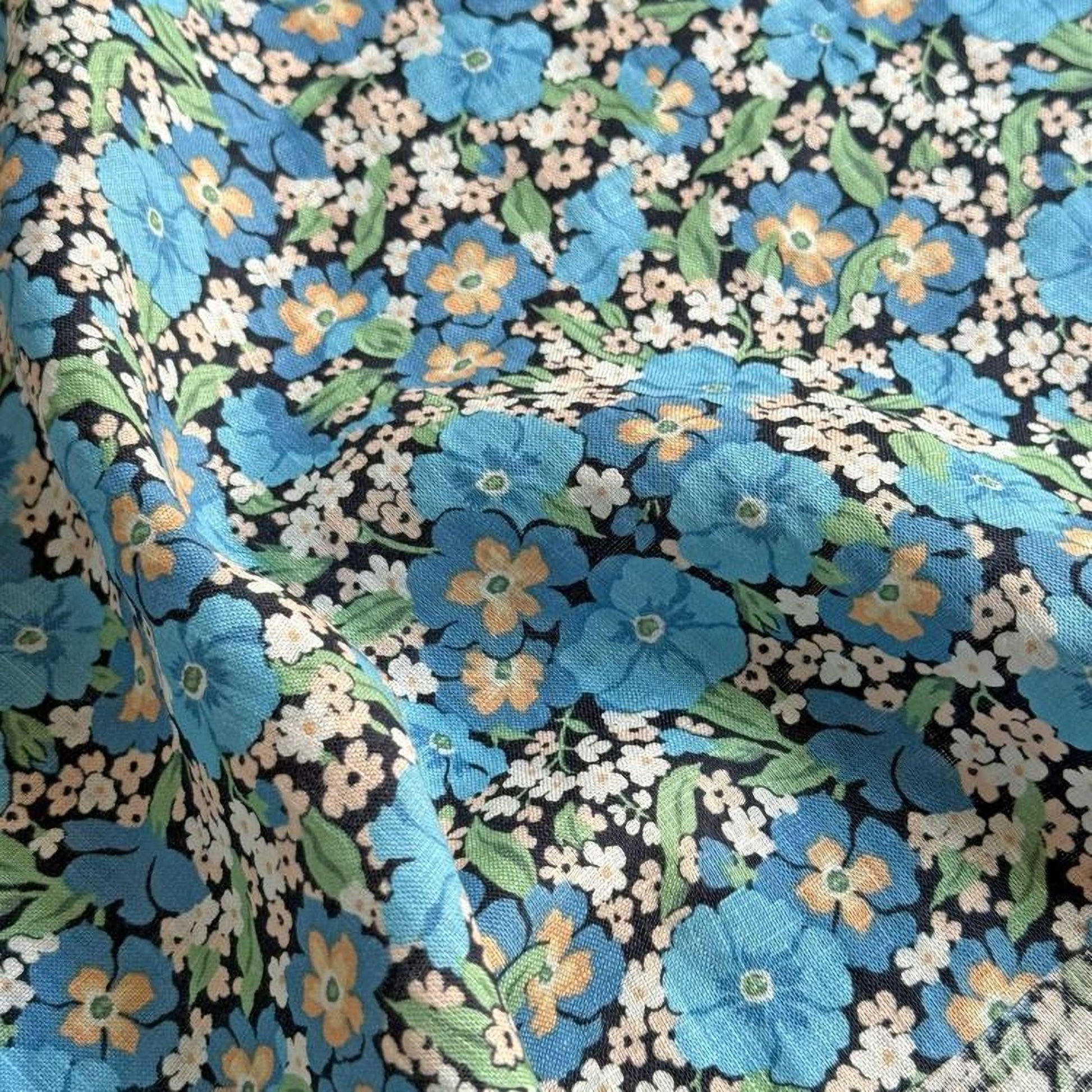 a close-up view of a fabric with a floral pattern. The fabric has a mix of blue and white flowers, along with green leaves, creating a vibrant and colorful design. The pattern appears to be a repeating floral motif, with the flowers and leaves arranged in a way that fills the entire fabric. The fabric has a textured appearance, suggesting it is made of a soft, plush material.