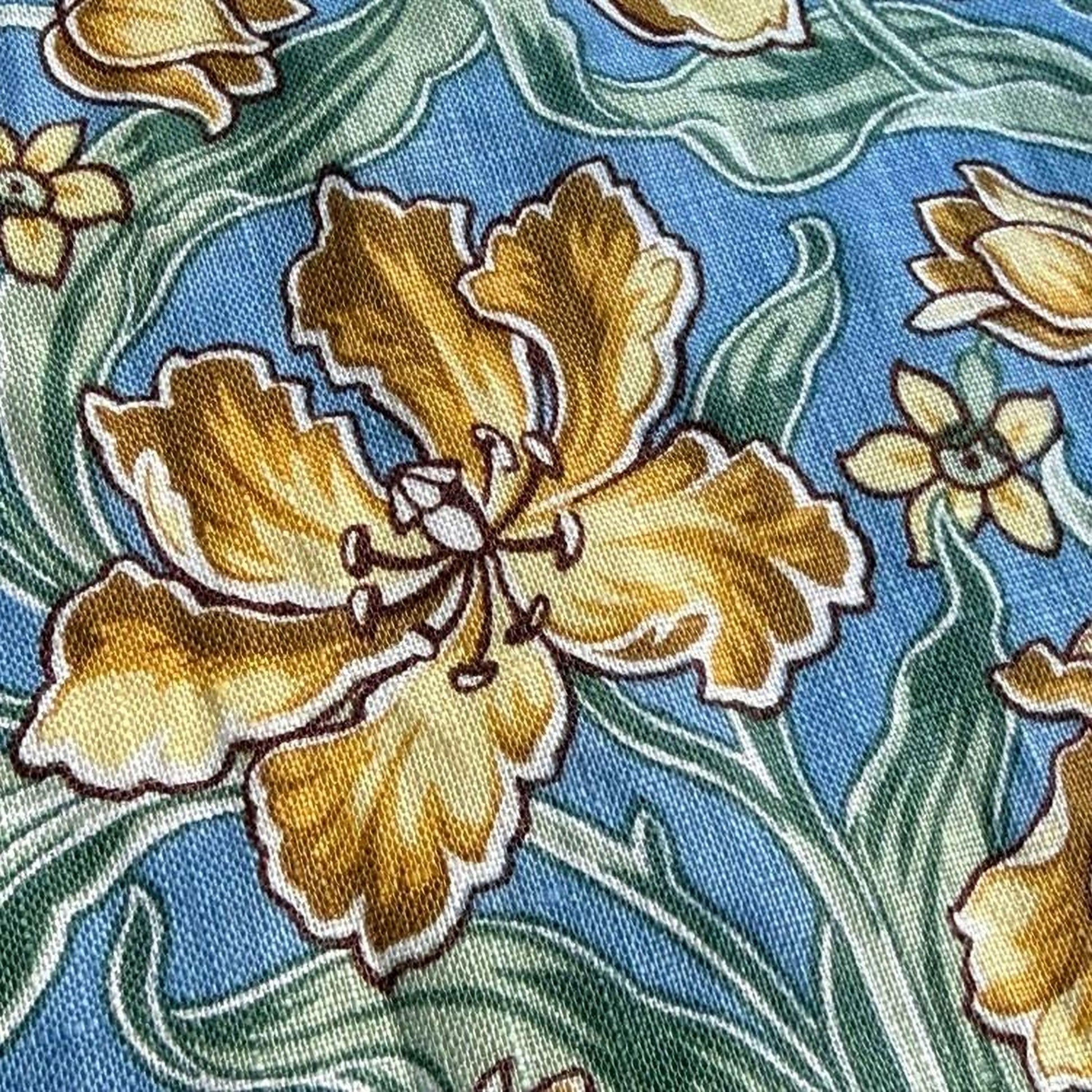a close-up view of a fabric with a floral pattern. The fabric has a blue background with yellow flowers and green leaves. The flowers are the main focus of the image, with one large yellow flower in the center and smaller yellow flowers surrounding it. The green leaves are scattered throughout the fabric, adding to the overall floral design.