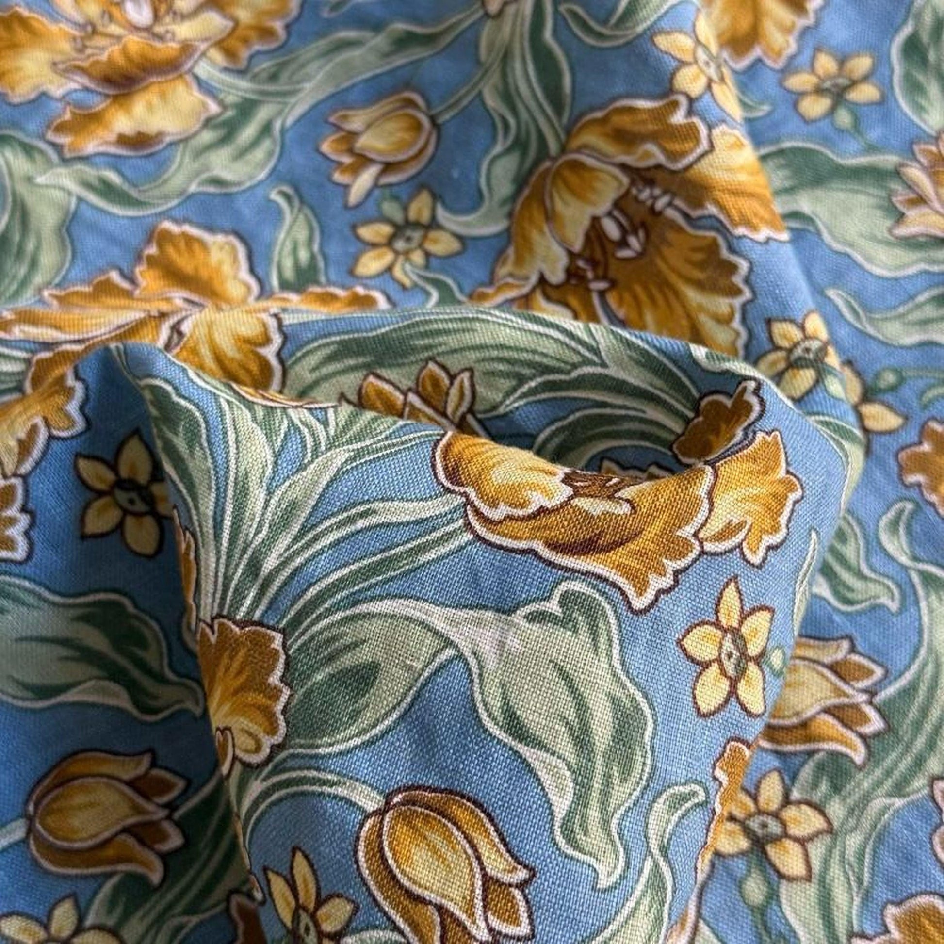 a close-up view of a fabric with a floral pattern in shades of blue and yellow. The fabric appears to be made of a soft, textured material, and the pattern features a variety of flowers and leaves in different sizes and colors.