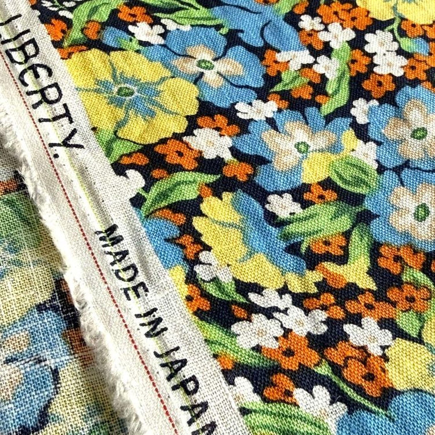 a close-up view of a fabric with a vibrant floral pattern in shades of blue, yellow, and orange. The fabric appears to be made in Japan, as indicated by the text "MADE IN JAPAN" visible on the fabric.