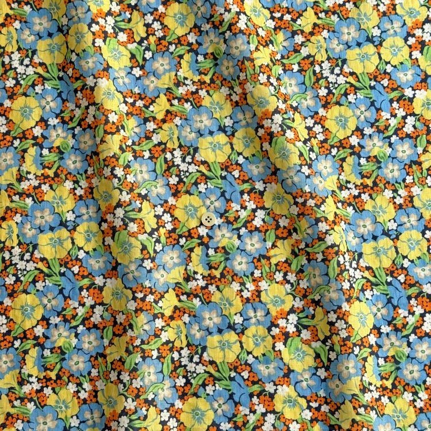 The image is a close-up view of a fabric with a vibrant floral pattern. The fabric is adorned with a variety of colorful flowers, including yellow, blue, and orange blooms, interspersed with green leaves. The pattern is intricate and detailed, showcasing the craftsmanship of the fabric.