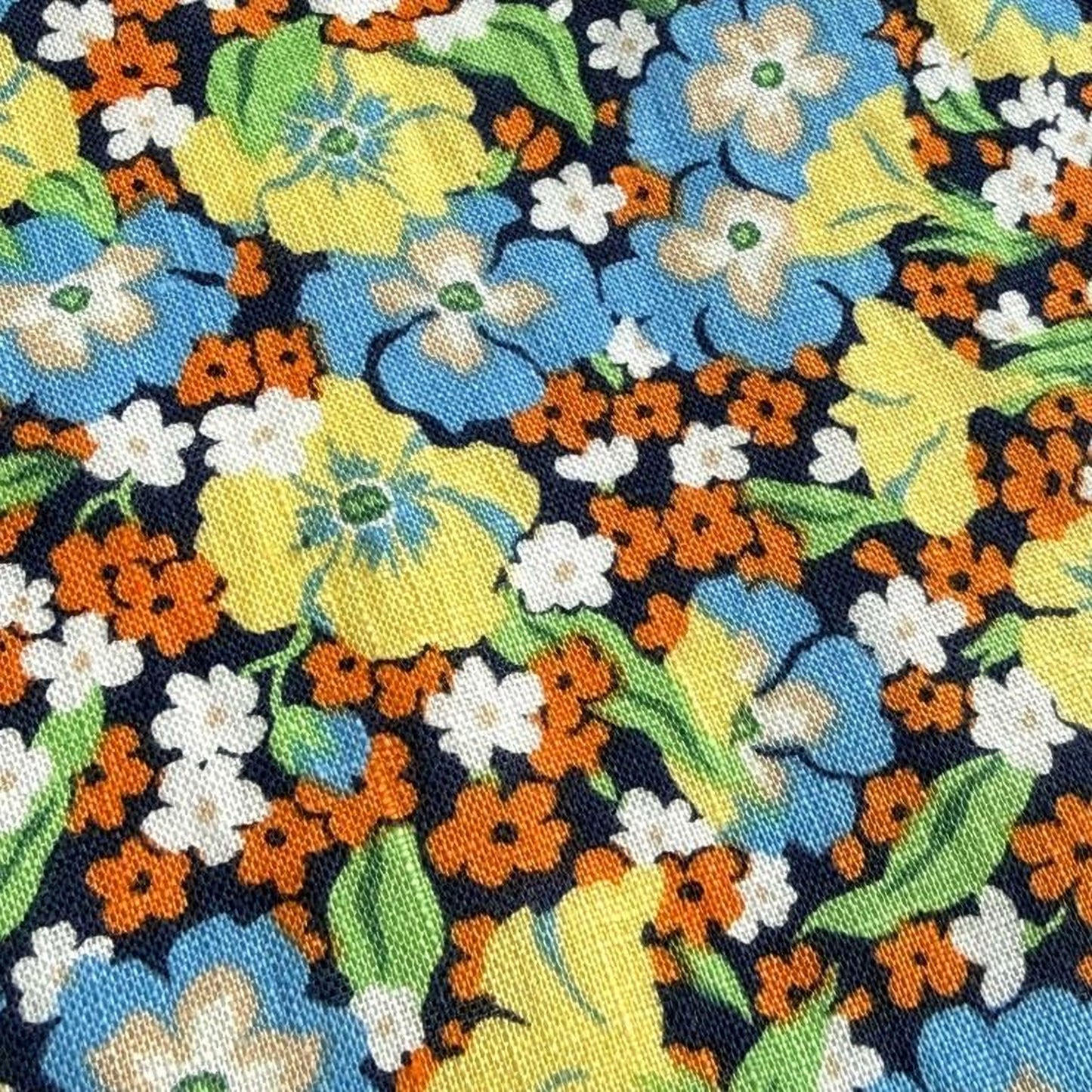 The image is a close-up of a fabric with a vibrant floral pattern in various colors, including yellow, orange, blue, and white.