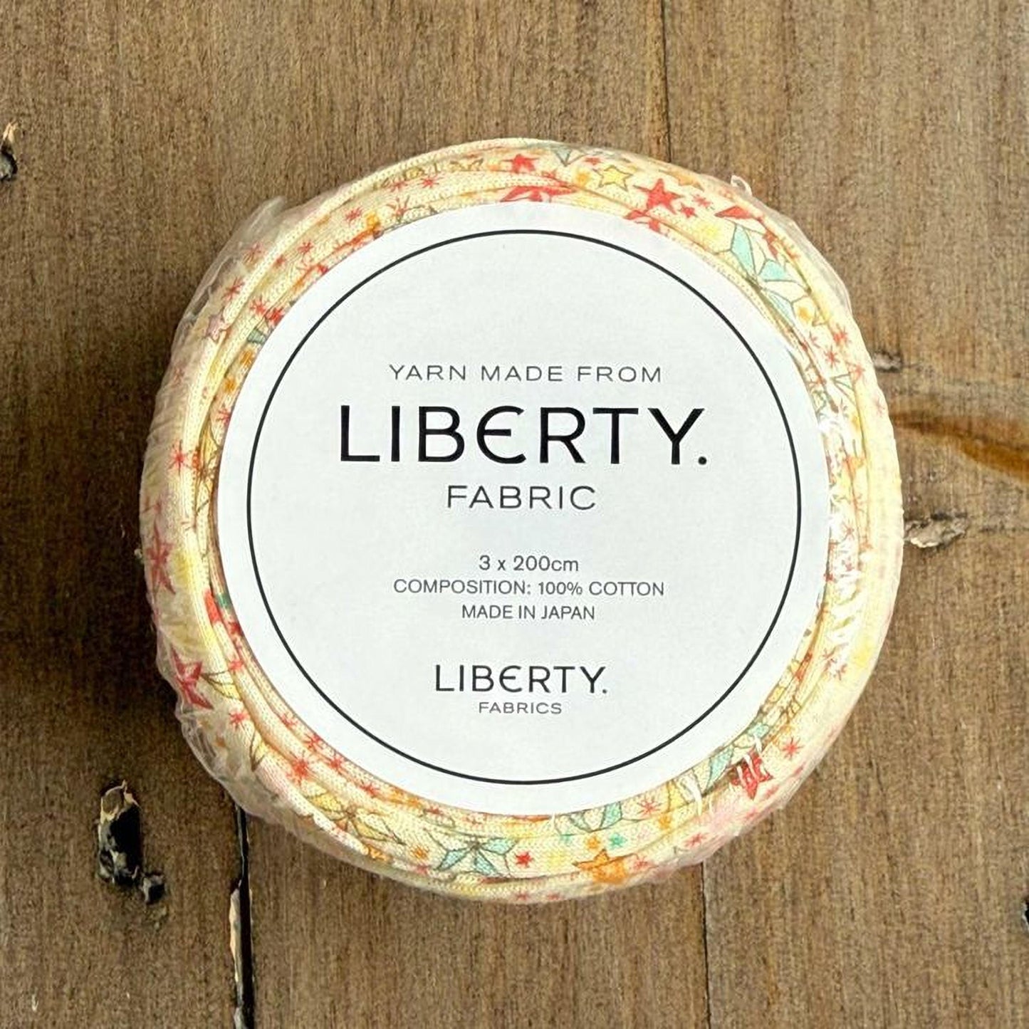 A circular container with a label that reads "Yarn Made from LIBERTY. FABRIC" and "3 x 200cm COMPOSITION: 100% COTTON MADE IN JAPAN LIBERTY FABRICS".