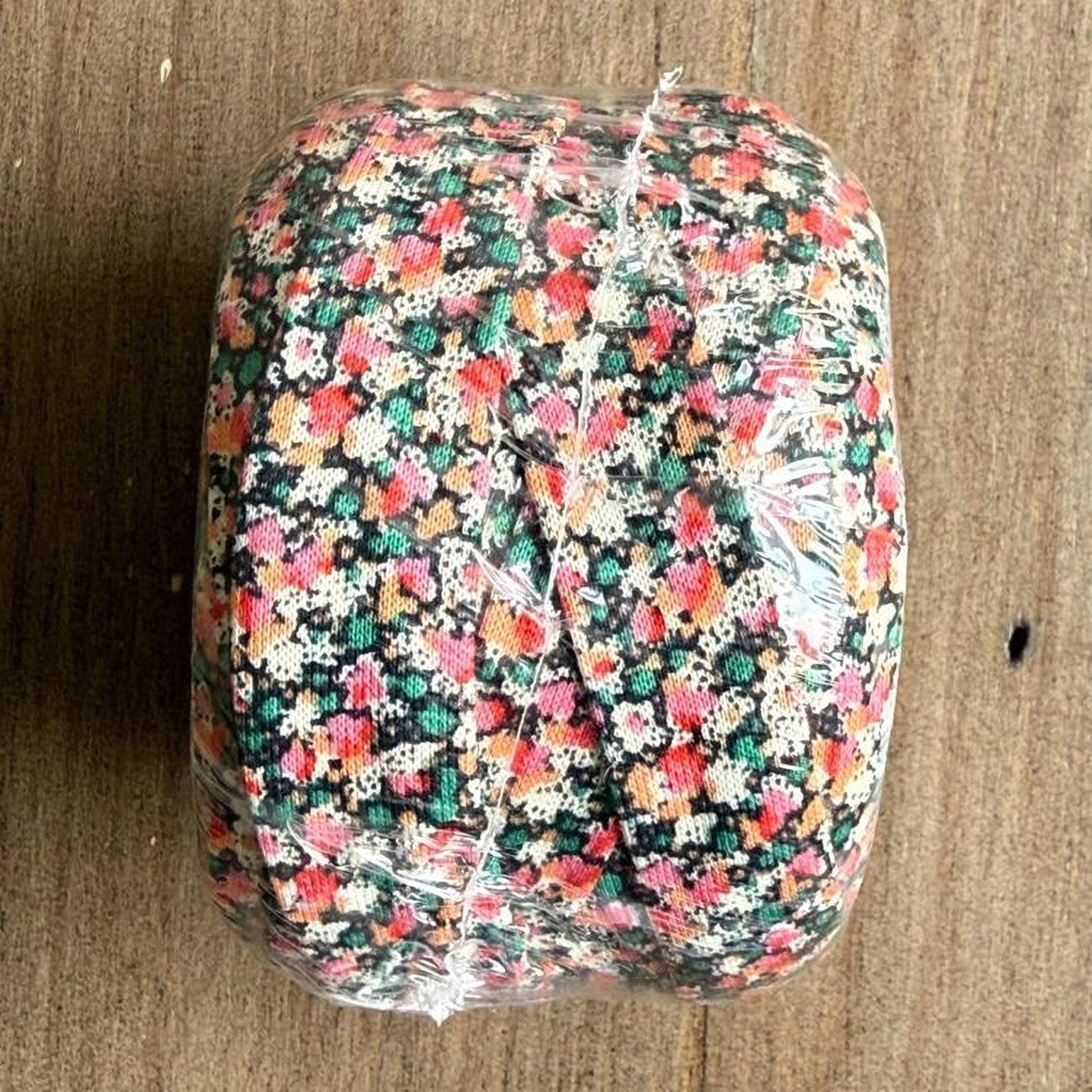 A colorful, floral-patterned object wrapped in plastic, sitting on a wooden surface.