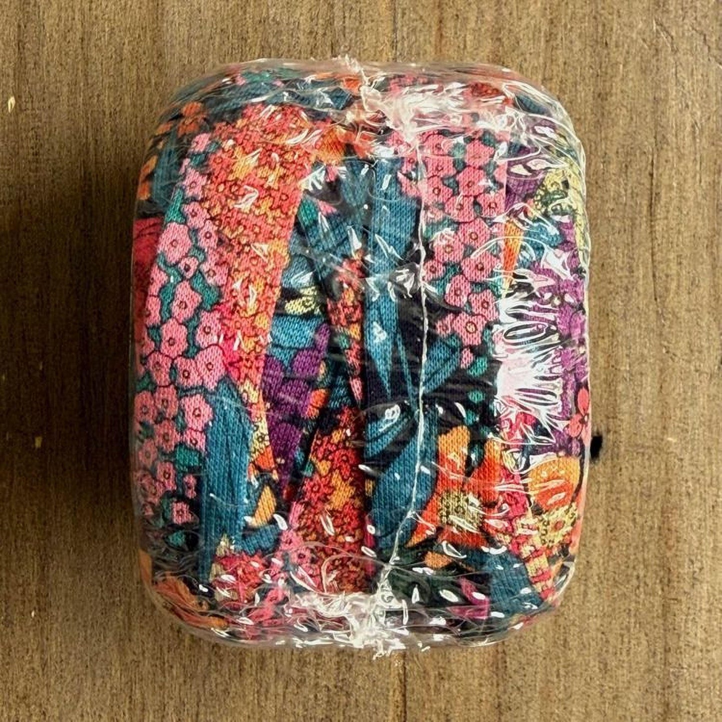 A colorful, floral-patterned object wrapped in plastic, sitting on a wooden surface.
