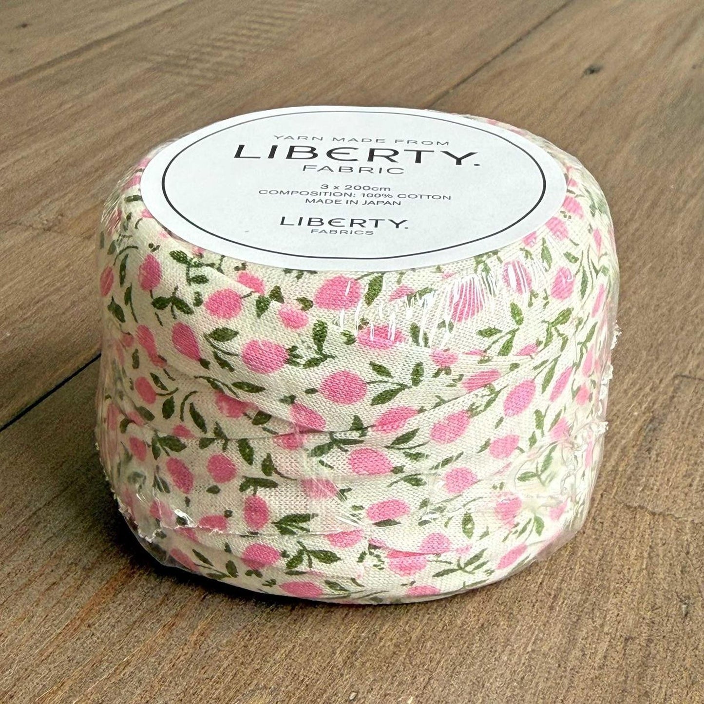 A roll of fabric with a floral pattern, labeled as "Liberty Fabric" and "Made from 100% Cotton".