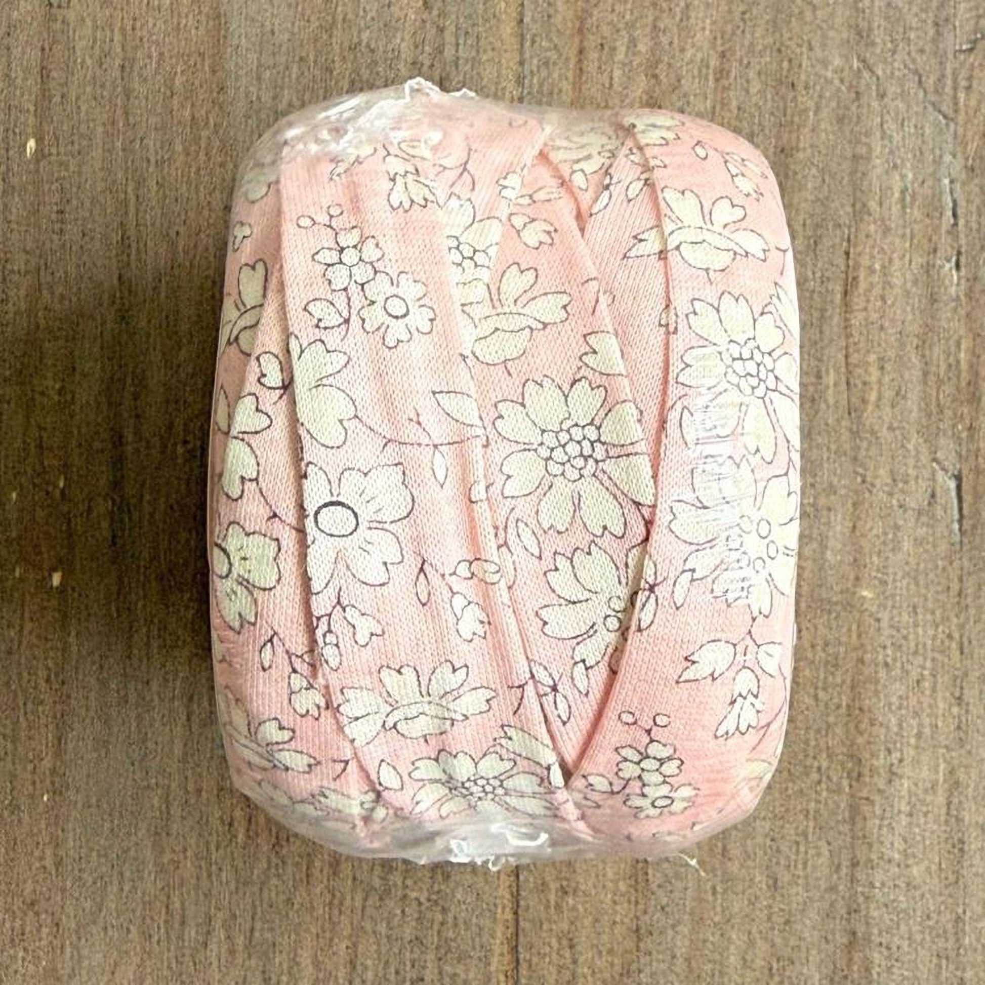 A roll of pink and white floral fabric is placed on a wooden surface.